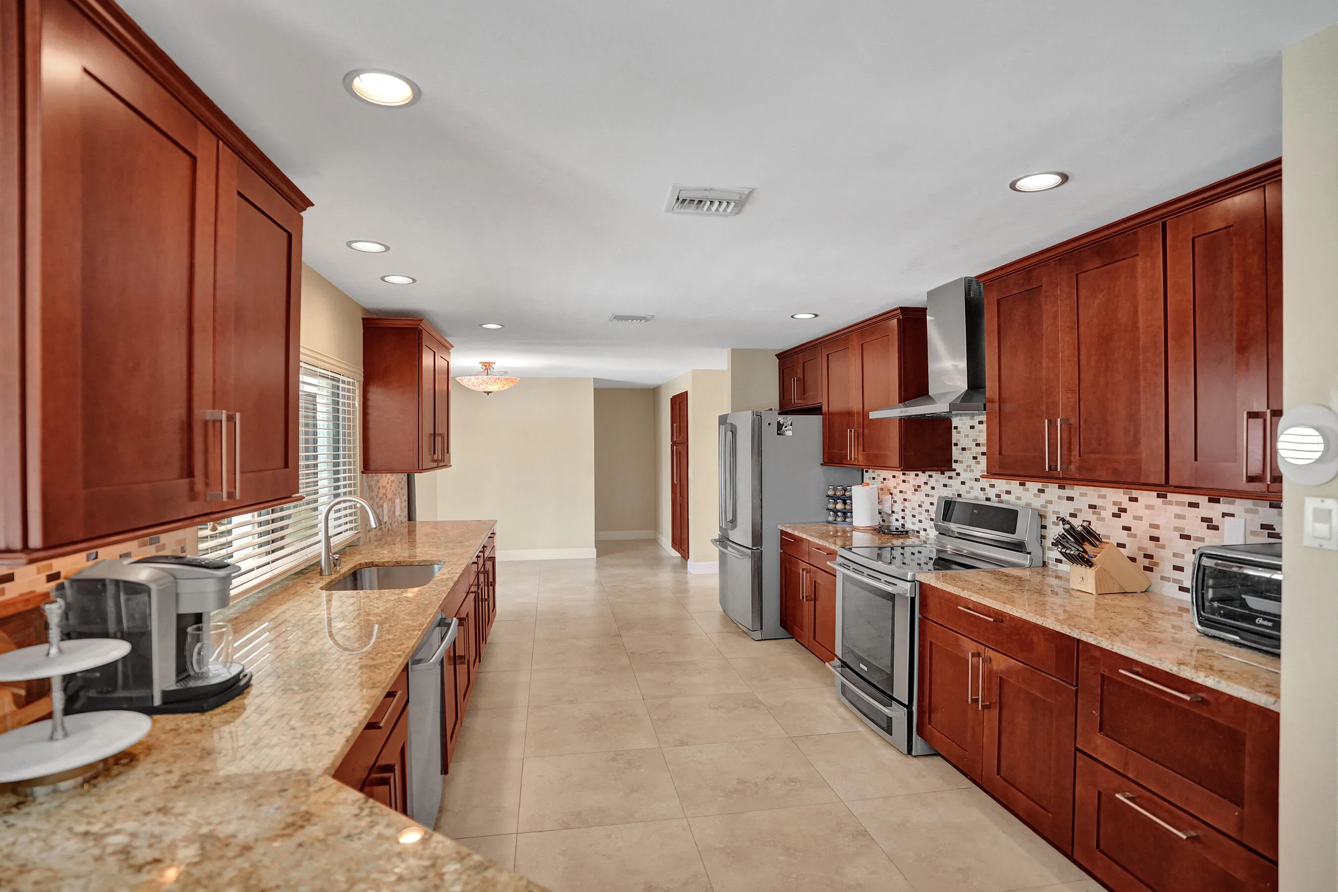 Kitchen featuring abundant wood-finish cabinetry, light-toned countertops, stainless steel appliances, a mosaic tile backsplash, and recessed lighting