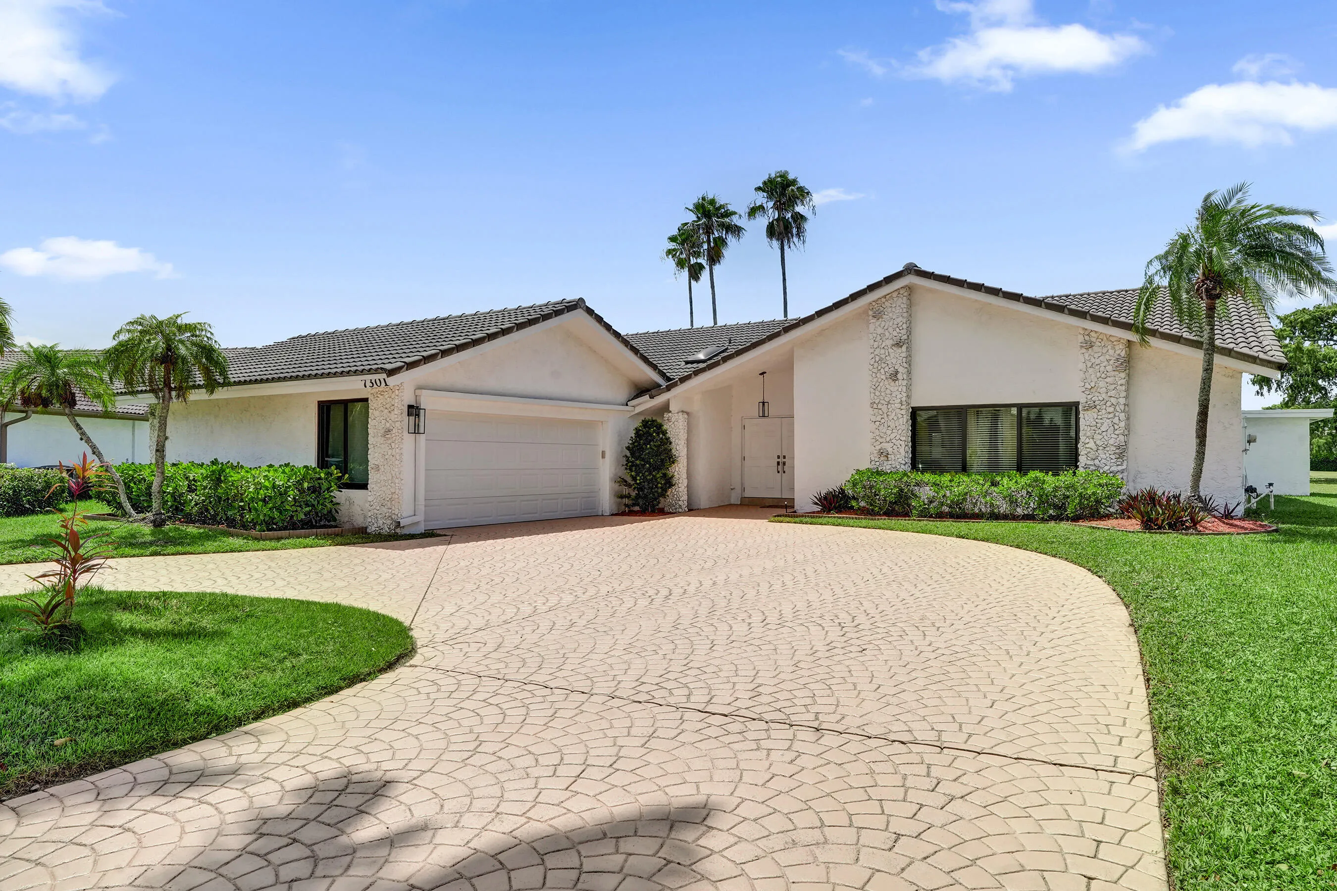 Contemporary stucco exterior with a tiled roof, decorative stone accents, a paver driveway, an attached garage, and manicured landscaping