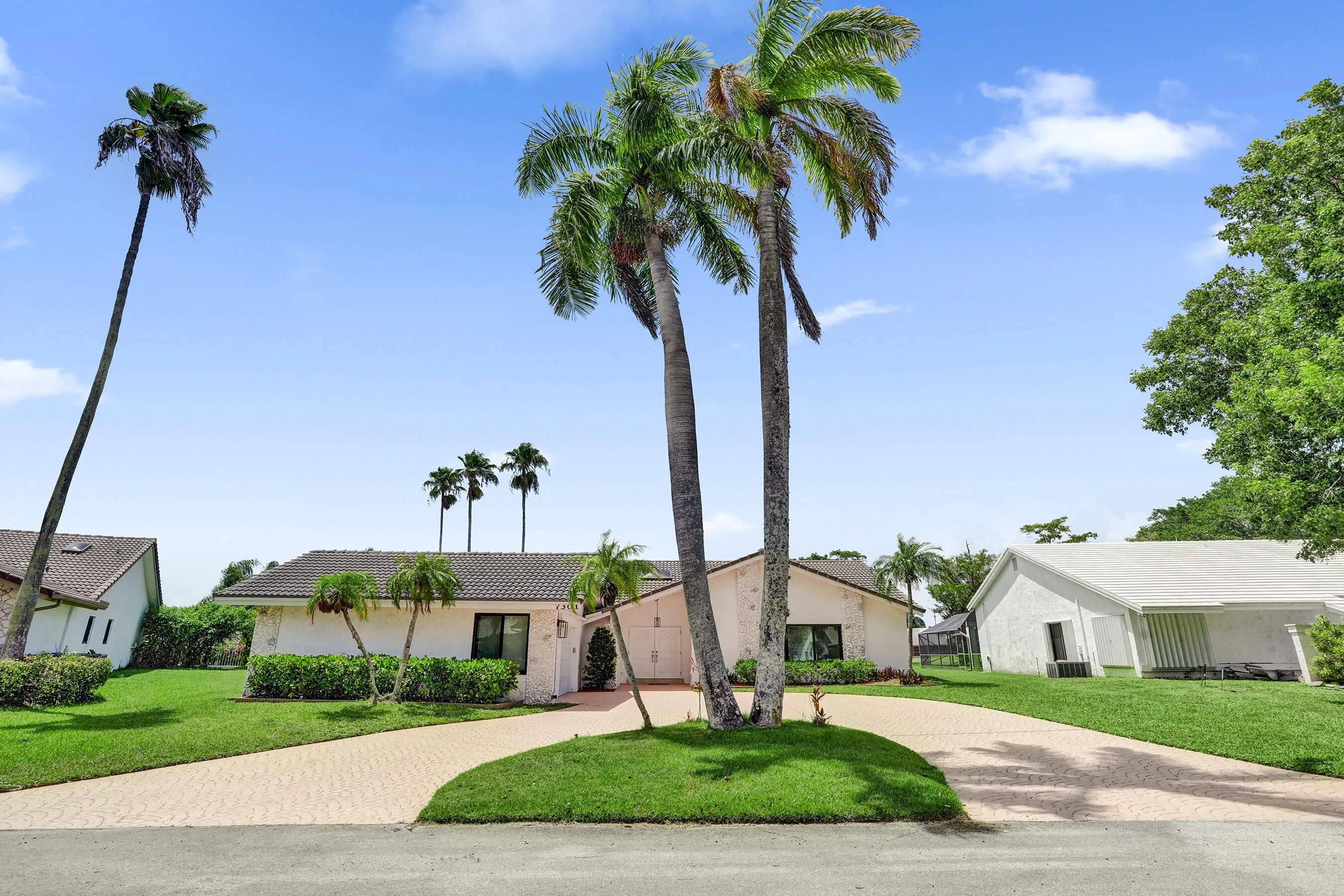 Manicured lawn with mature palm trees, a paver driveway, and a residence with a tiled roof