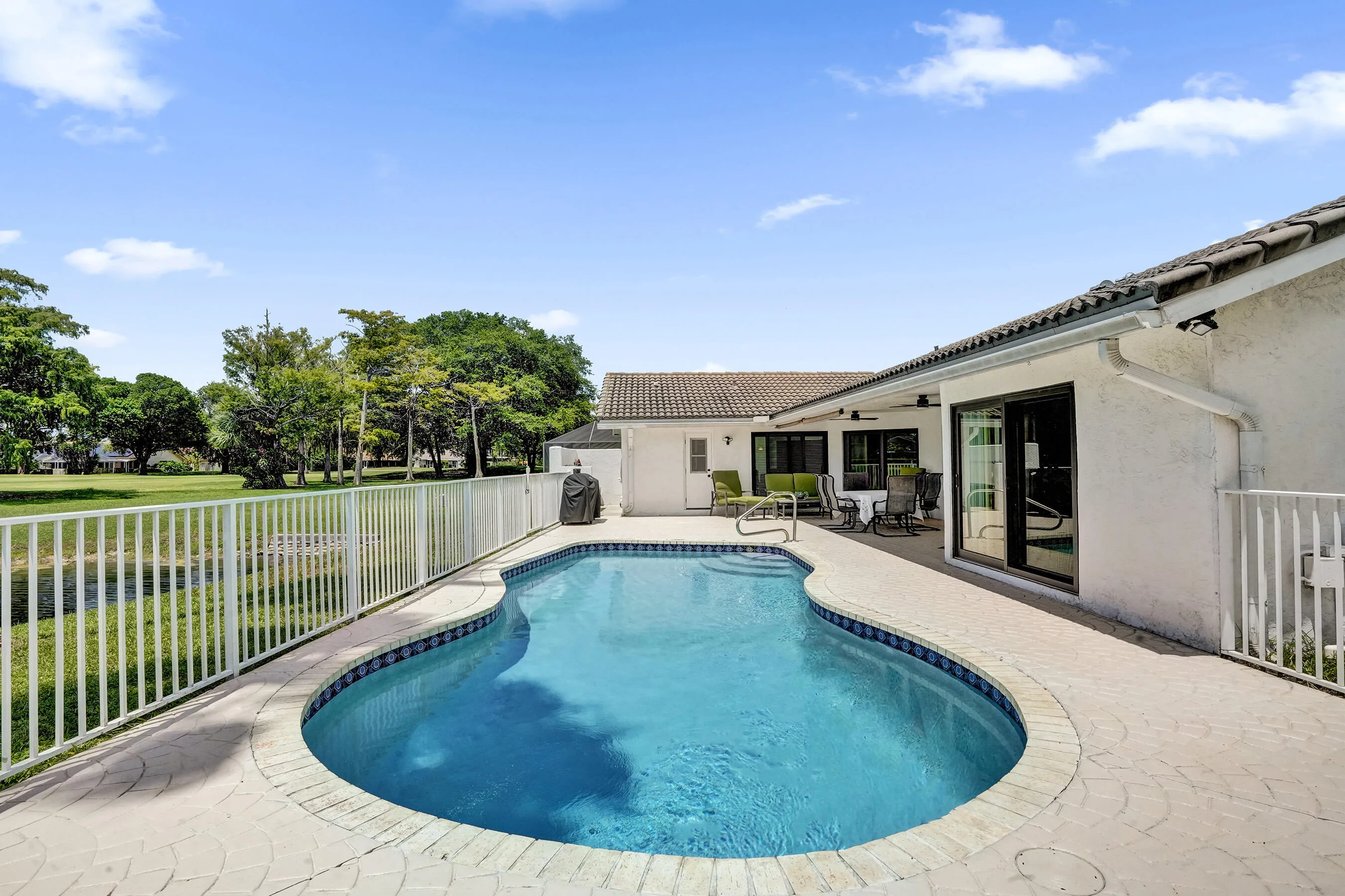 Freeform swimming pool with a tiled border and integrated steps, surrounded by a stamped concrete patio