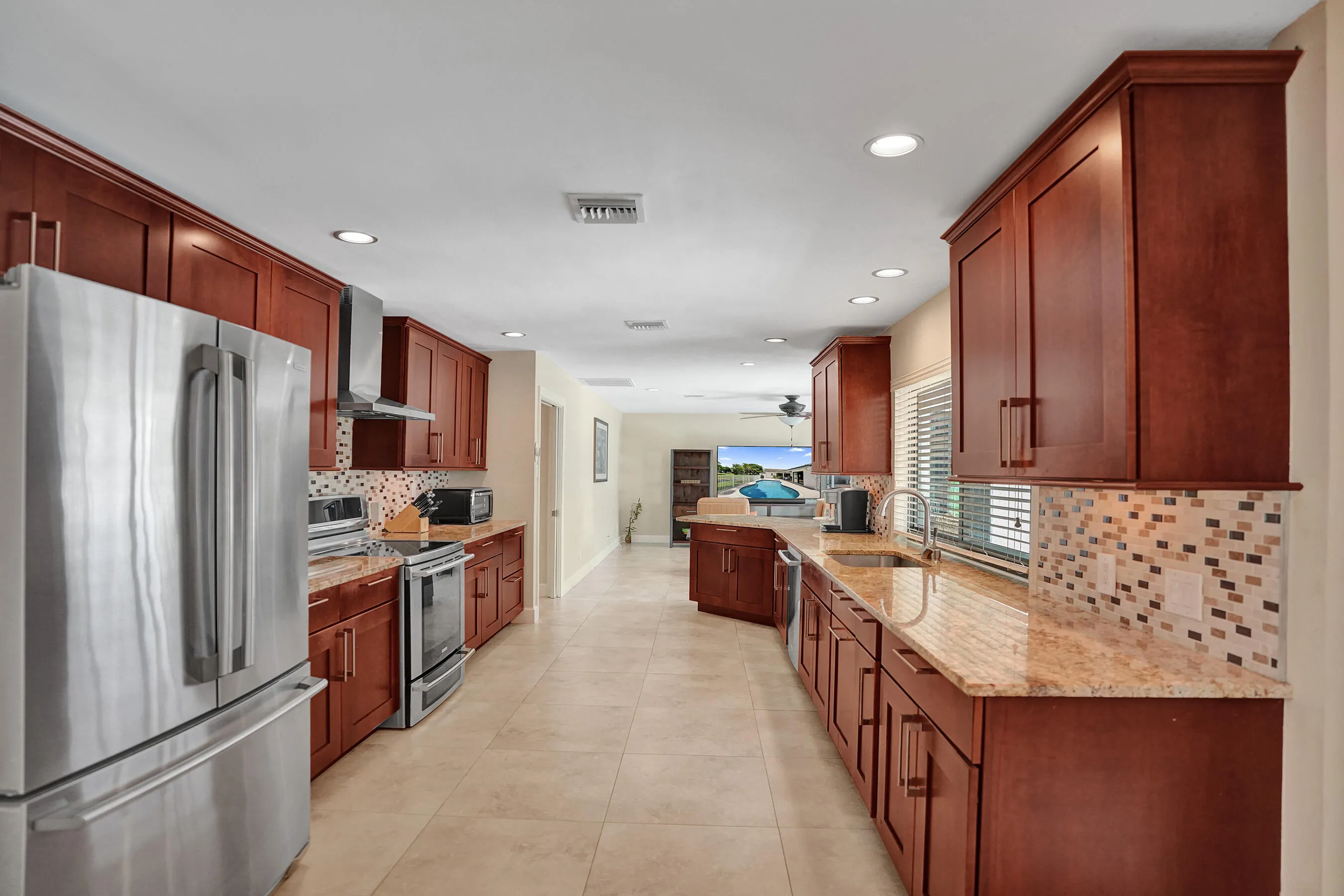 Spacious kitchen with wood cabinetry, stainless steel appliances, mosaic tile backsplash, polished countertops, and recessed lighting