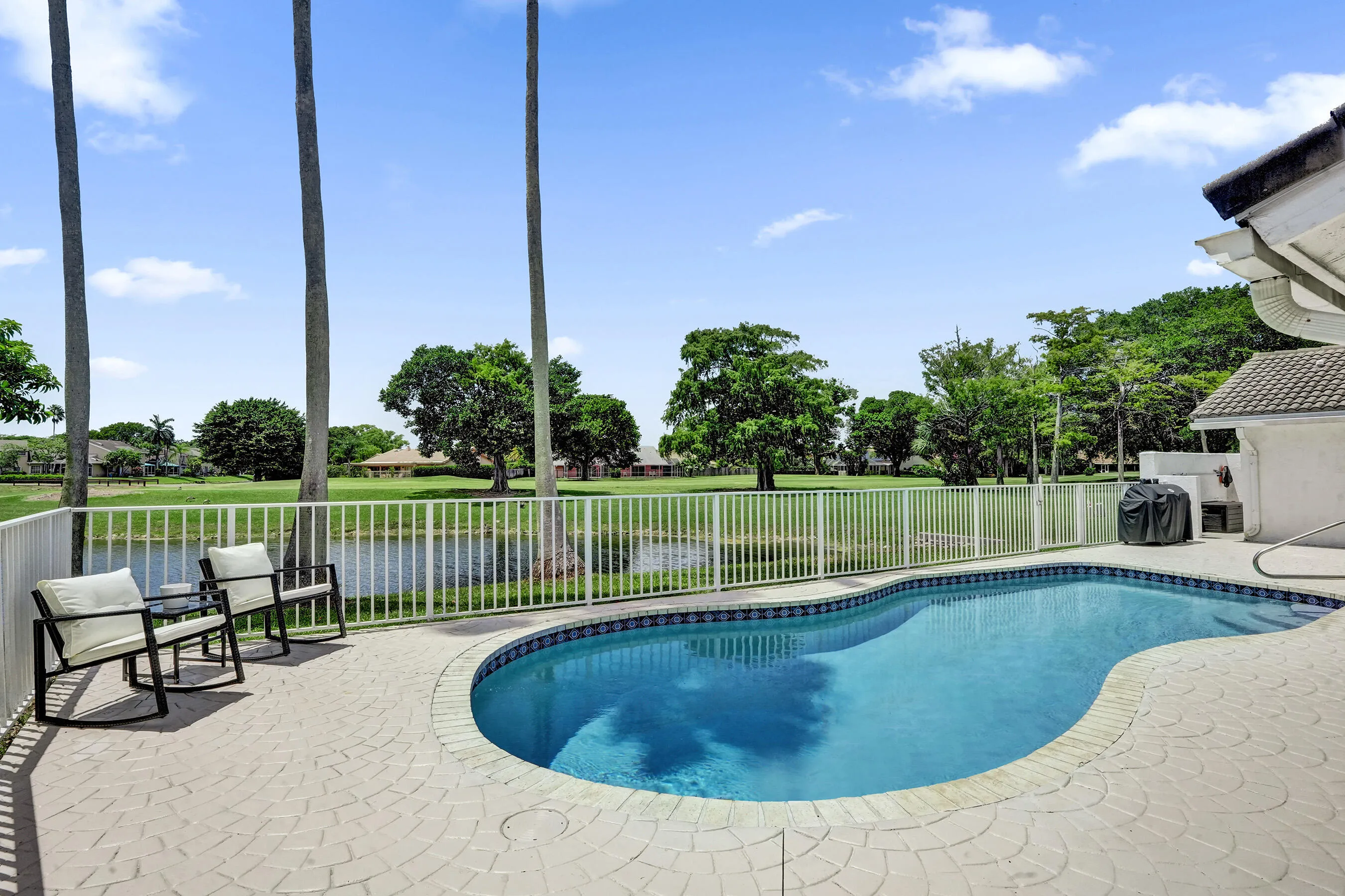 Freeform swimming pool with tiled border, paver patio, and white perimeter fencing