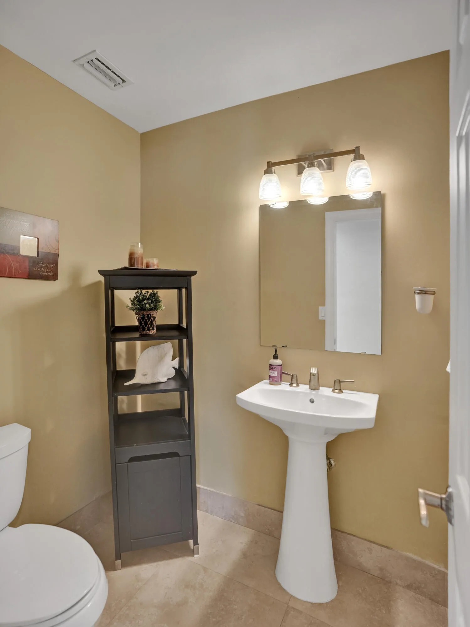 Pedestal sink with a wall-mounted mirror and three-light vanity fixture