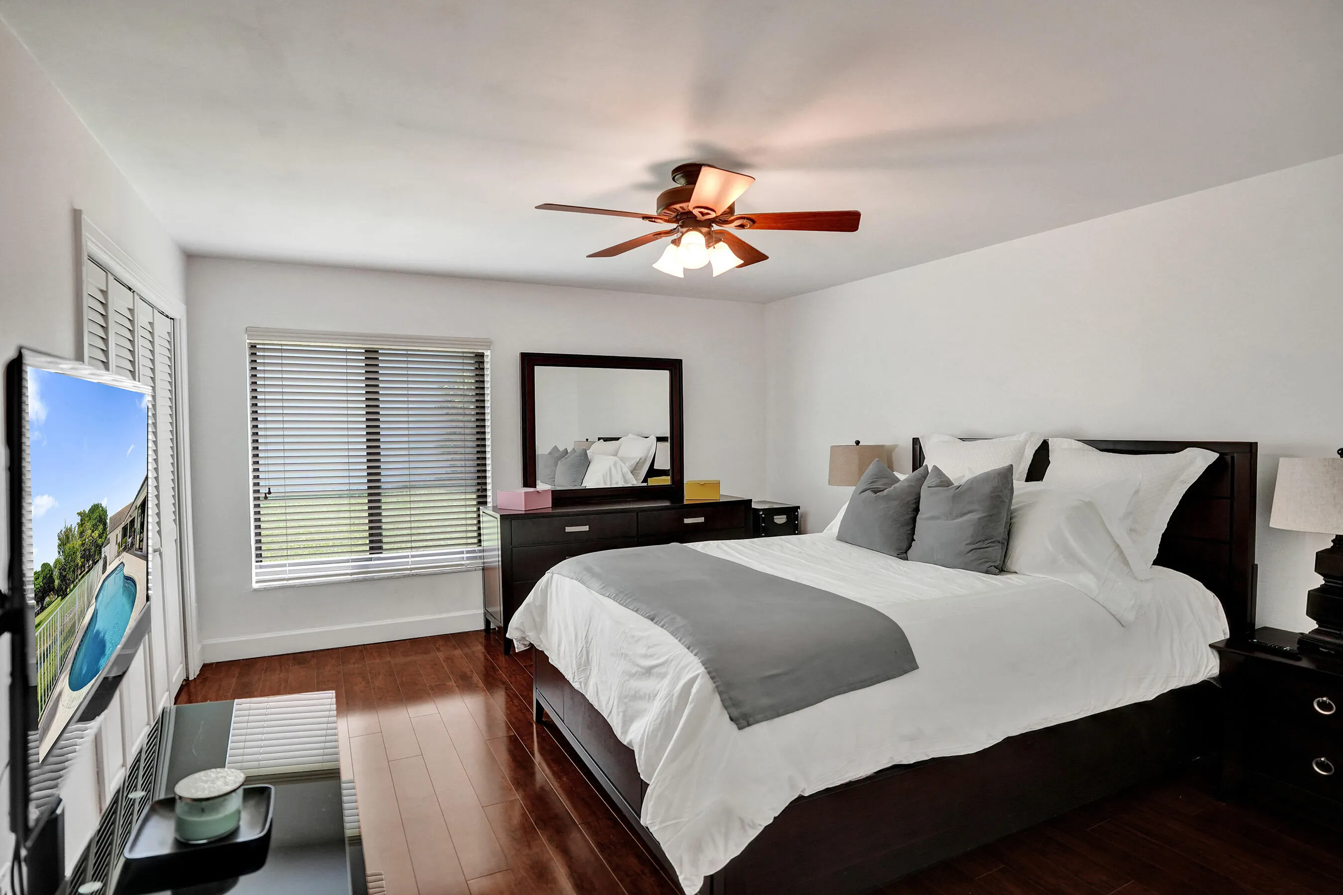 Wood-finish flooring throughout, modern ceiling fan with integrated lighting, window with horizontal blinds, built-in closet with louvered doors