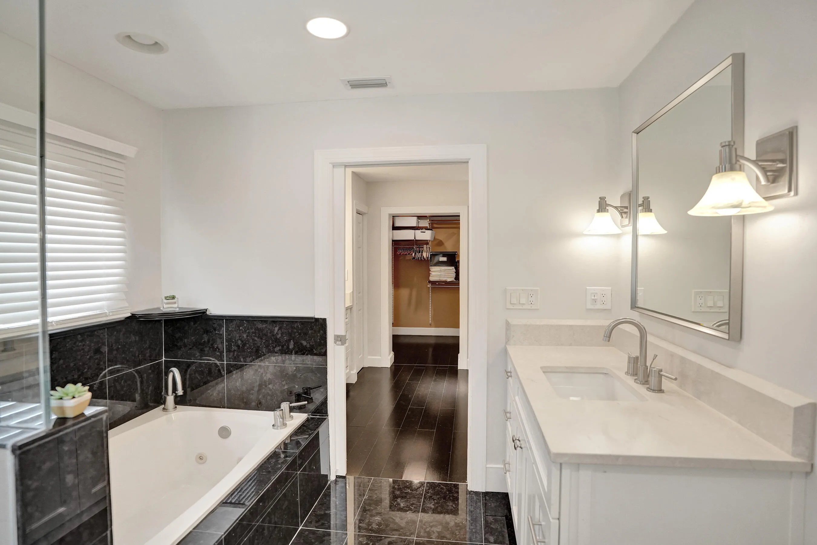 Recessed lighting, wood-finish flooring, built-in soaking tub, vanity with integrated sink, and wall-mounted sconces