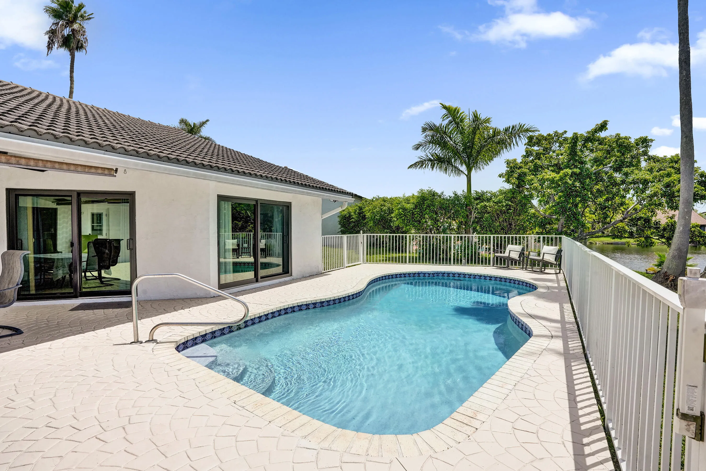 Curved swimming pool with a surrounding paver patio, accessible via sliding glass doors