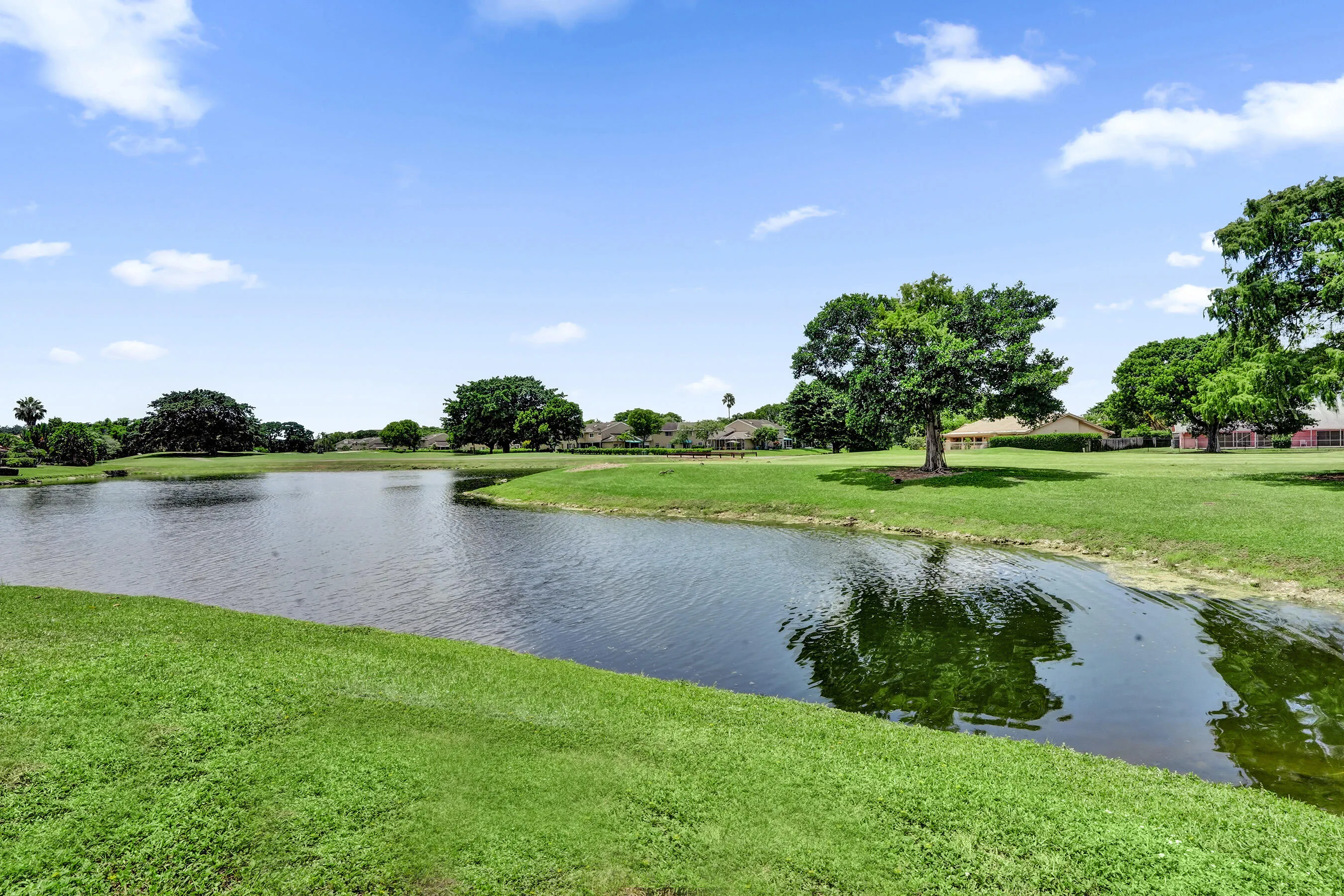 Expansive green space featuring a serene pond, mature trees, and natural landscaping
