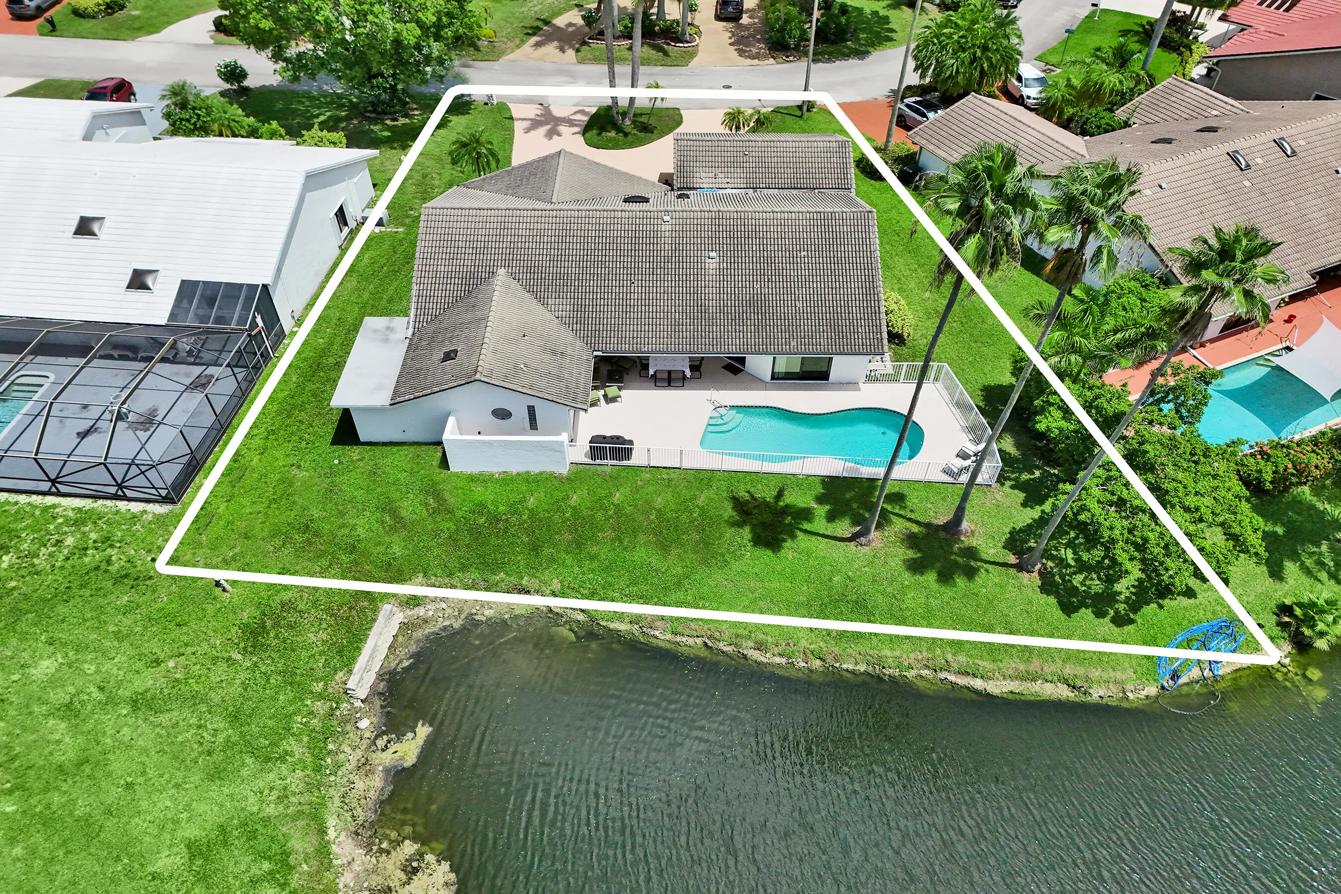 Waterfront property featuring a private swimming pool, expansive patio, mature palm trees, and a spacious green lawn