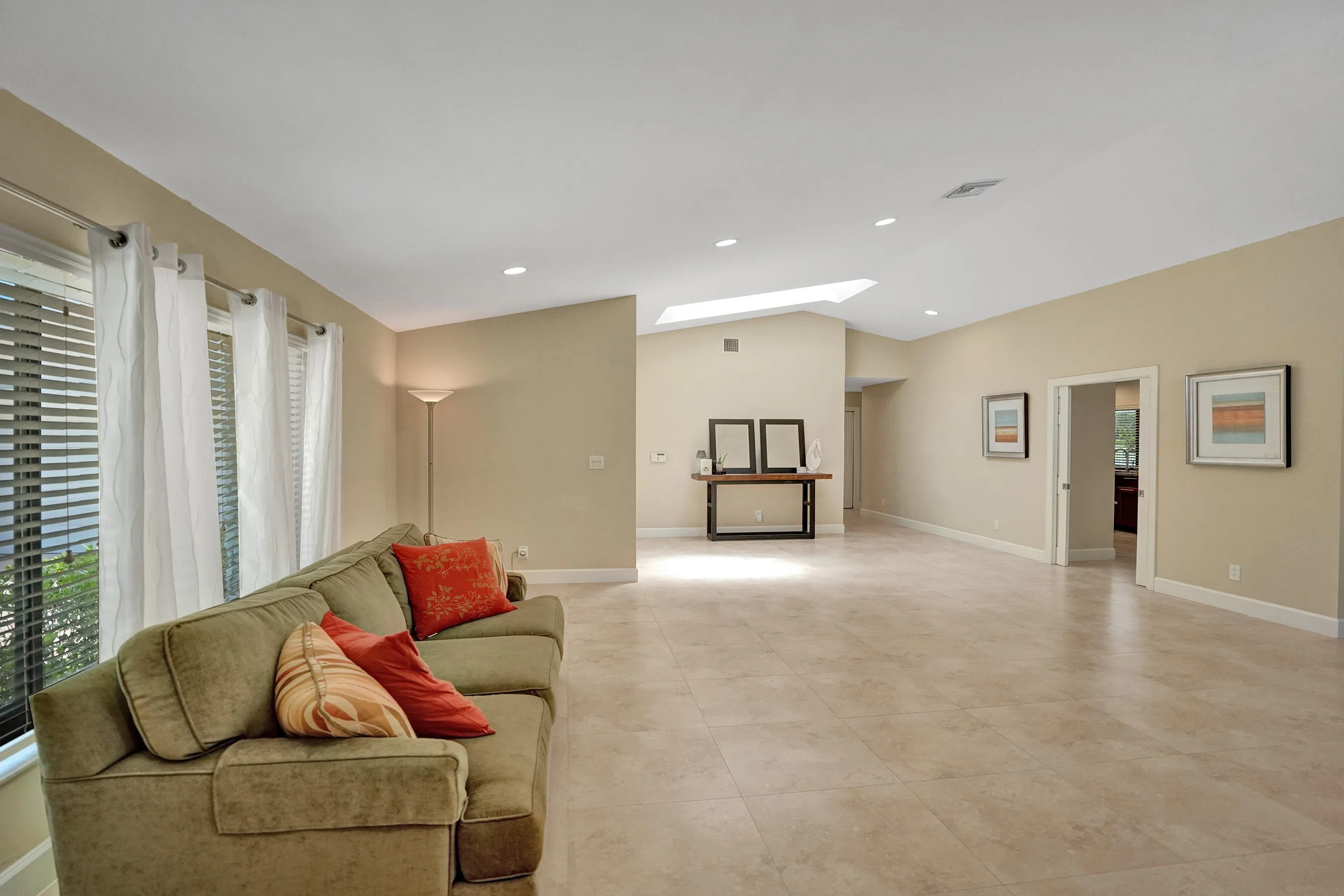 Vaulted ceiling with skylight, recessed lighting, expansive tiled flooring, and multiple window openings