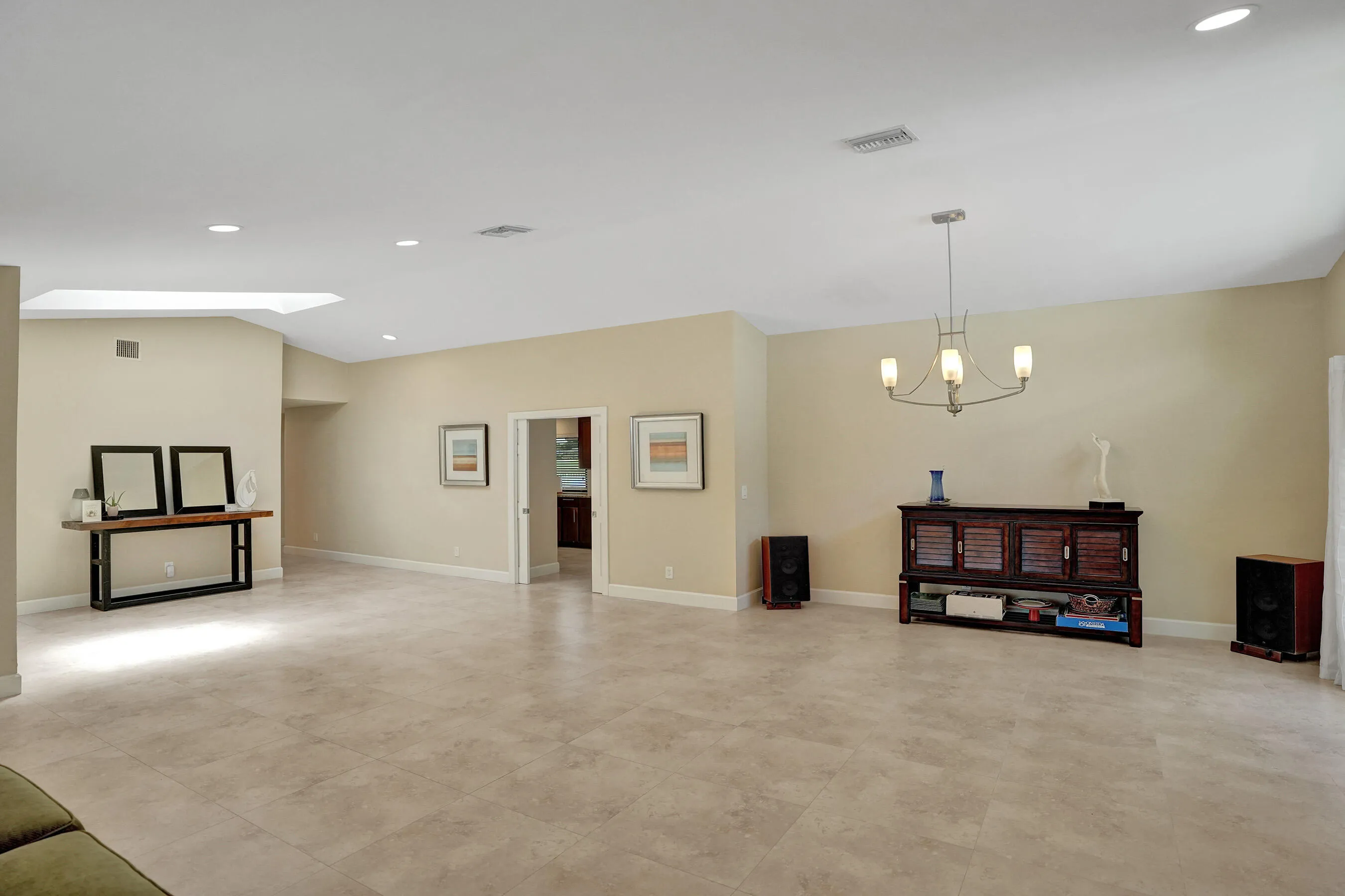 Spacious room featuring tile flooring, a vaulted ceiling, recessed lighting, a skylight, and a chandelier