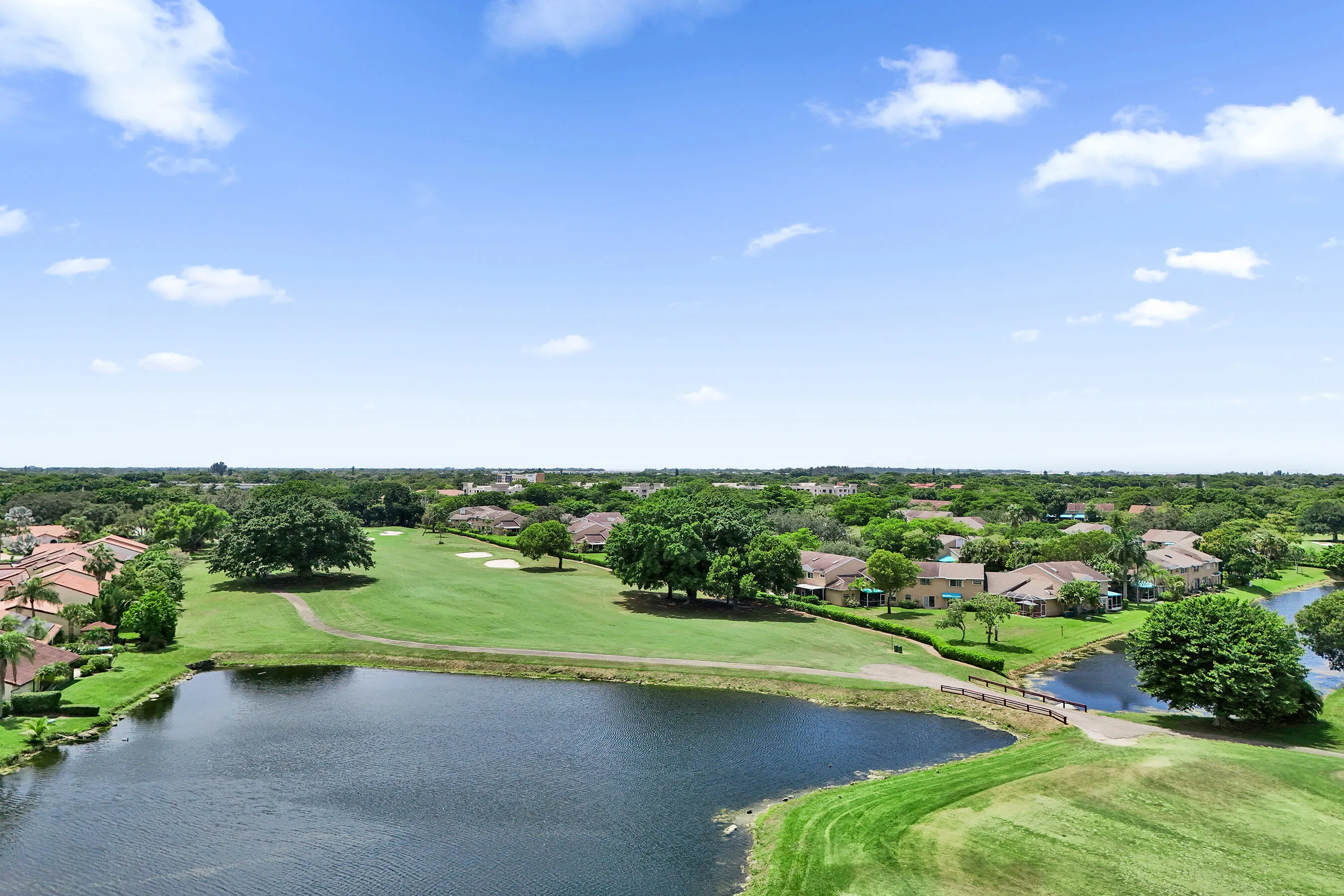 Expansive golf course frontage with a manicured green, mature trees, and a tranquil pond with a connecting bridge