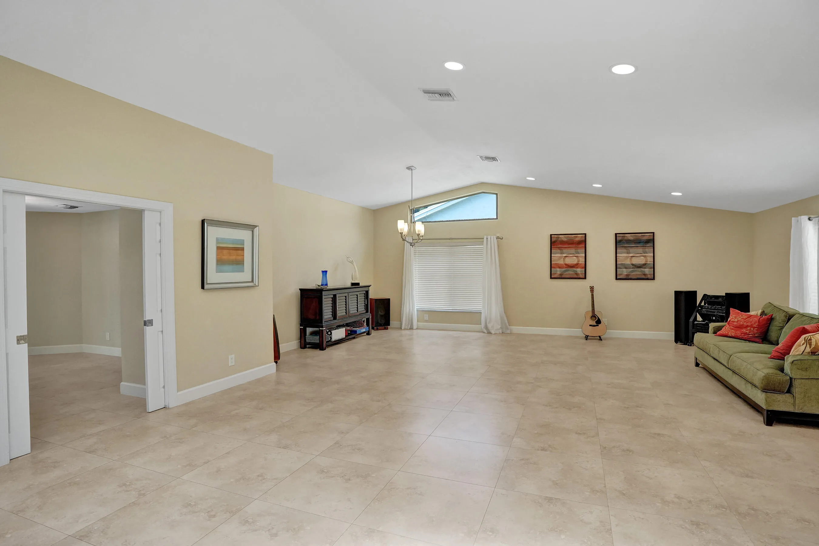 Spacious living area featuring vaulted ceilings, recessed lighting, tile flooring, and a large window with transom