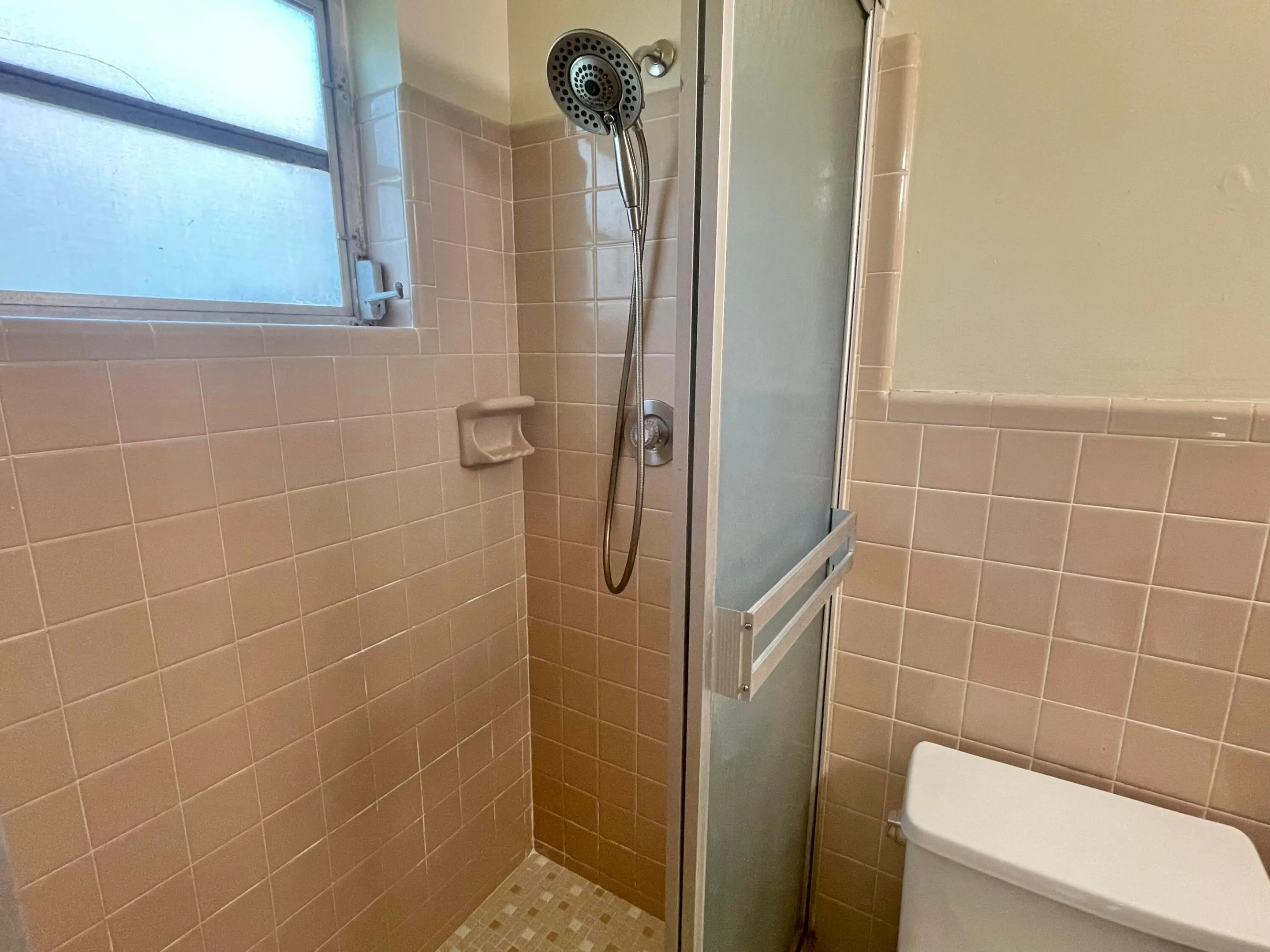 Shower enclosure with a frosted glass door, tiled walls, mosaic tile flooring, and a multi-function shower head