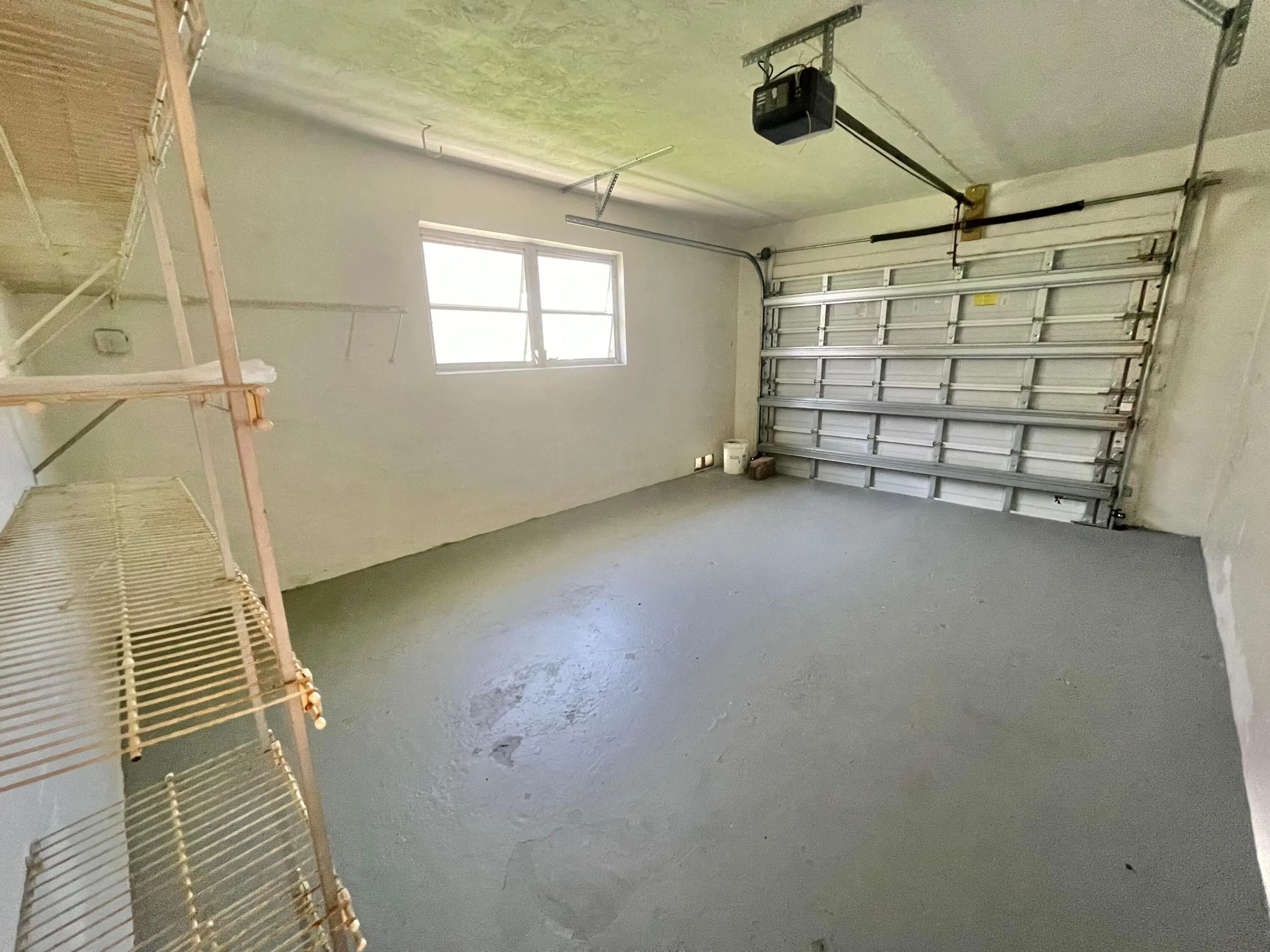 Spacious garage featuring polished concrete flooring, overhead garage door with automatic opener, high ceiling clearance, and natural light from transom window