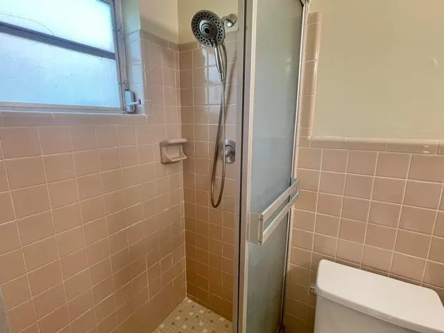 Shower enclosure with a frosted glass door, tiled walls, mosaic tile flooring, and a multi-function shower head