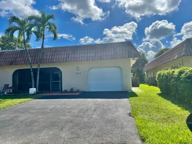 Stucco exterior with a tiled roof, attached garage, screened patio, and mature palm trees