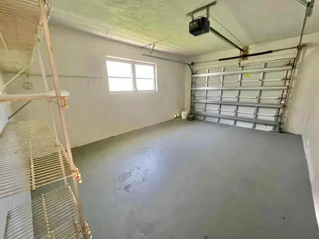 Spacious garage featuring polished concrete flooring, overhead garage door with automatic opener, high ceiling clearance, and natural light from transom window