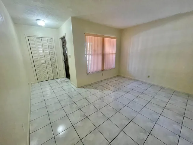 Tiled flooring throughout, louvered bi-fold closet doors, and a window with vertical blinds