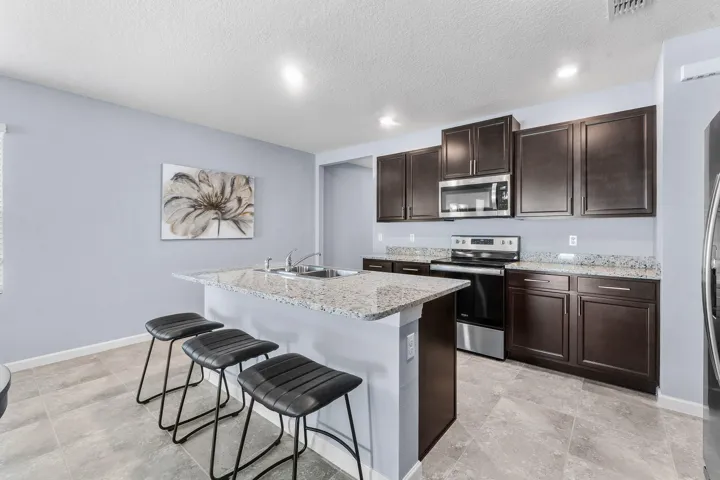 Kitchen featuring an island with a breakfast bar, granite countertops, stainless steel appliances, dark wood-finish cabinetry, and tile flooring