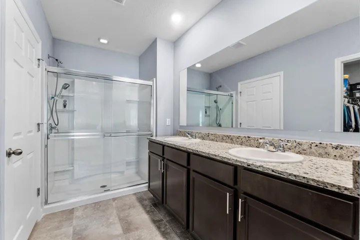 Double vanity with undermount sinks, granite-finish countertop, dark wood-finish cabinetry, and a glass-enclosed shower with sliding doors
