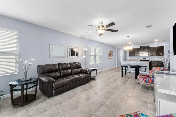 Open-concept living space with large format tile flooring, a ceiling fan, and multiple windows with blinds
