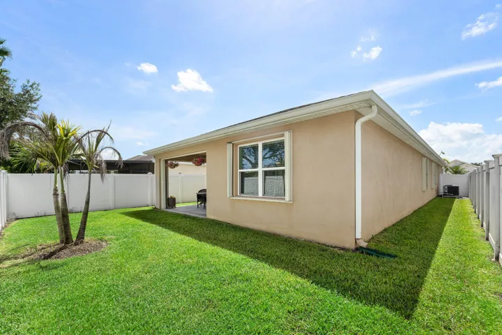 Expansive backyard with a manicured lawn, established palm trees, covered patio, and white PVC privacy fencing