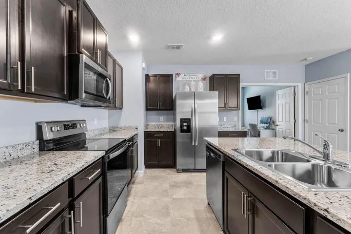 Kitchen featuring stainless steel appliances, dark wood-finish cabinetry, granite countertops, and tile flooring