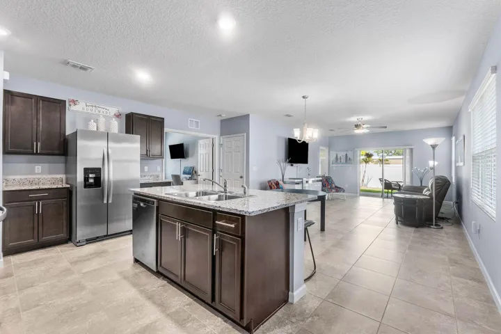 Kitchen island with double basin sink and granite-style countertop, stainless steel refrigerator and dishwasher, recessed lighting, and tile flooring