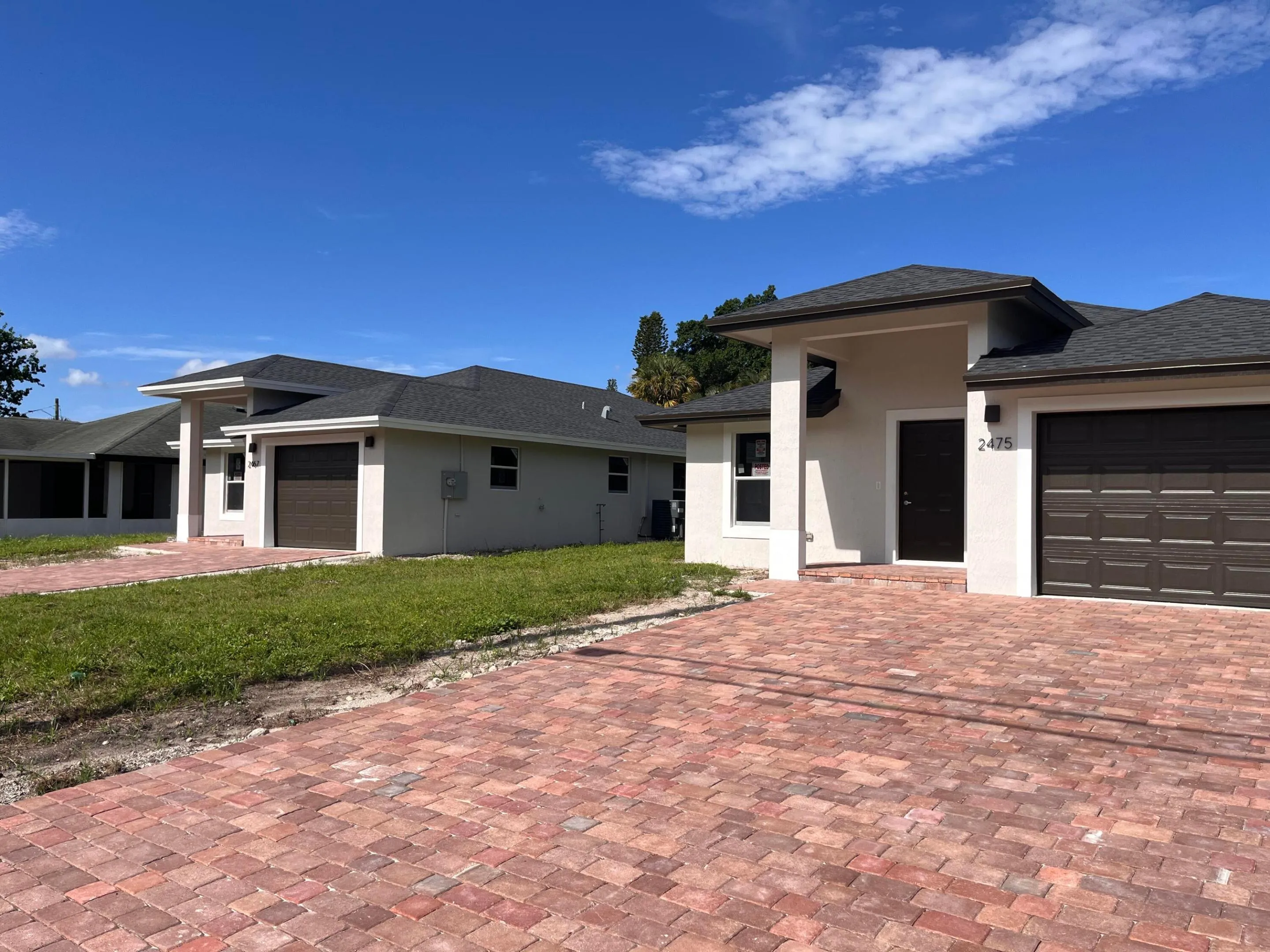 Contemporary stucco exterior with a dark shingle roof, integrated garage, covered entry, and a brick paver driveway