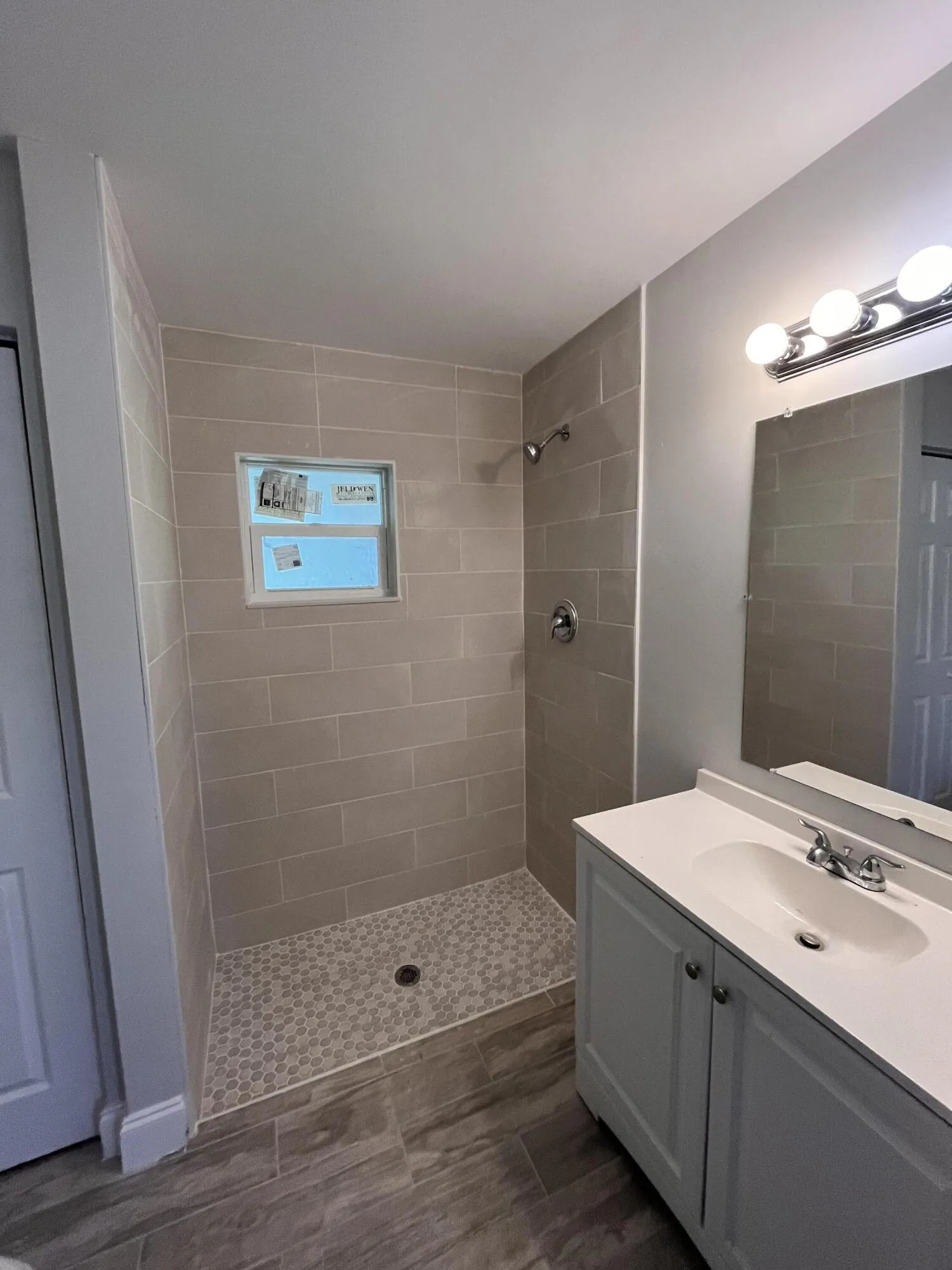 Walk-in shower with tiled walls and floor, single vanity with integrated sink, chrome fixtures, and wood-finish flooring