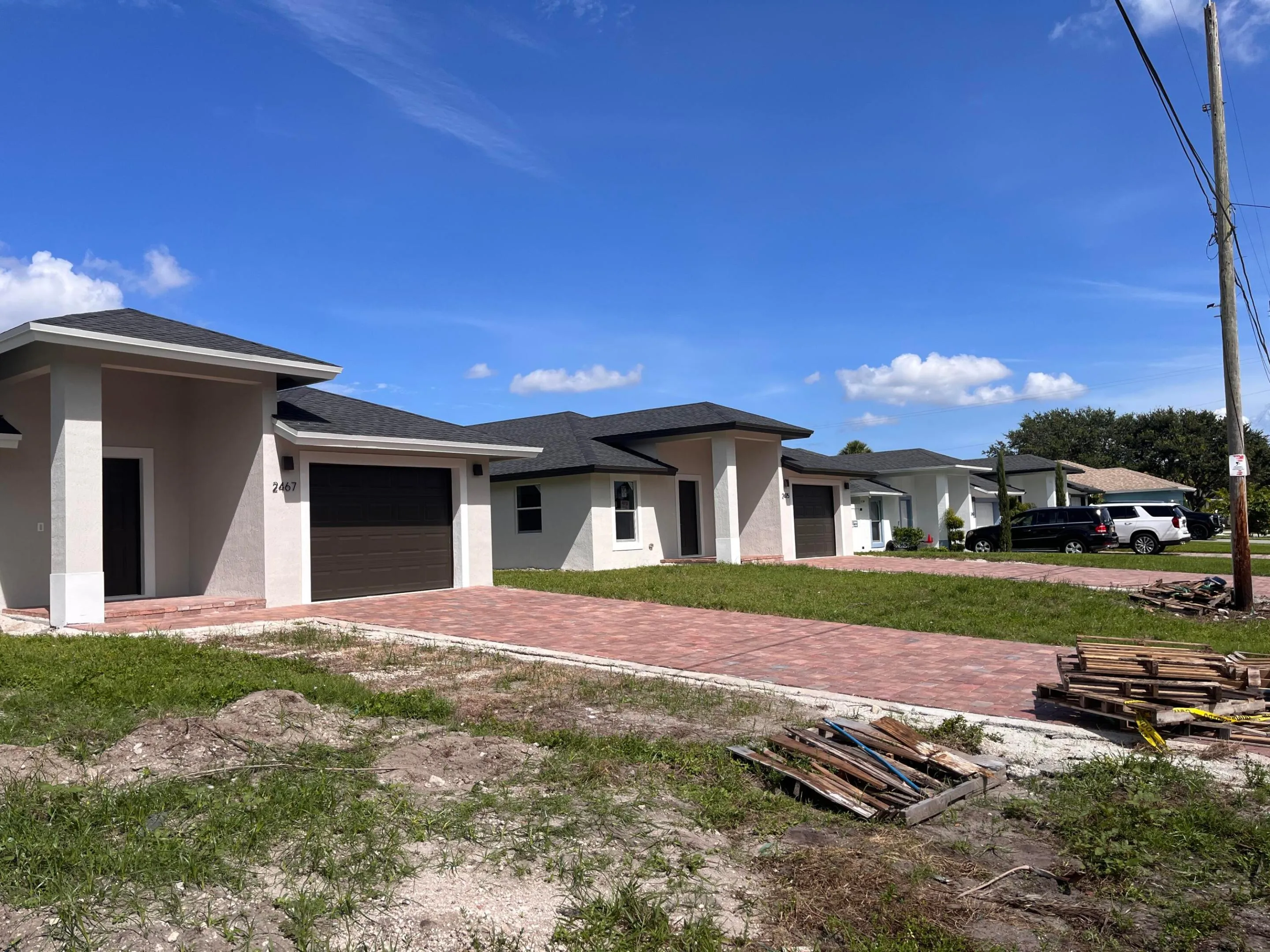 Modern stucco exterior with dark shingle roof, integrated garage, and brick paver driveway
