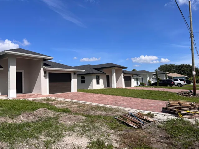 Modern stucco exterior with dark shingle roof, integrated garage, and brick paver driveway