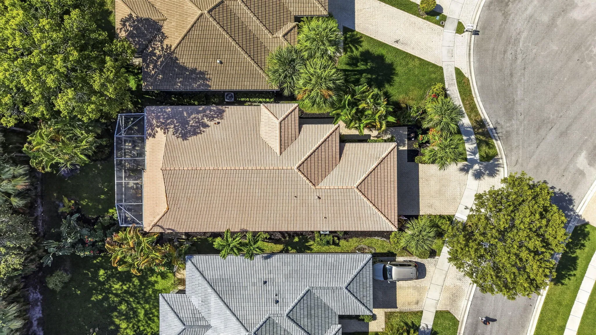 Terracotta tile roof with multiple gables, screened enclosure, concrete driveway, and a curved sidewalk