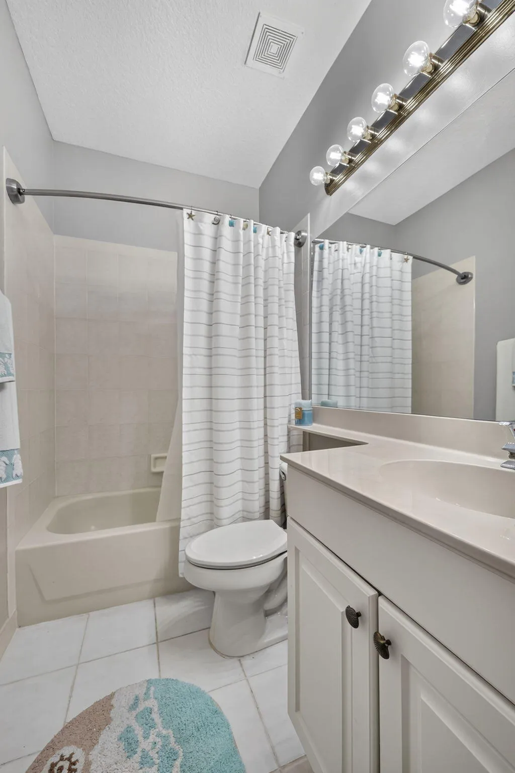 White vanity with dark hardware, integrated sink, large mirror, and overhead vanity lighting