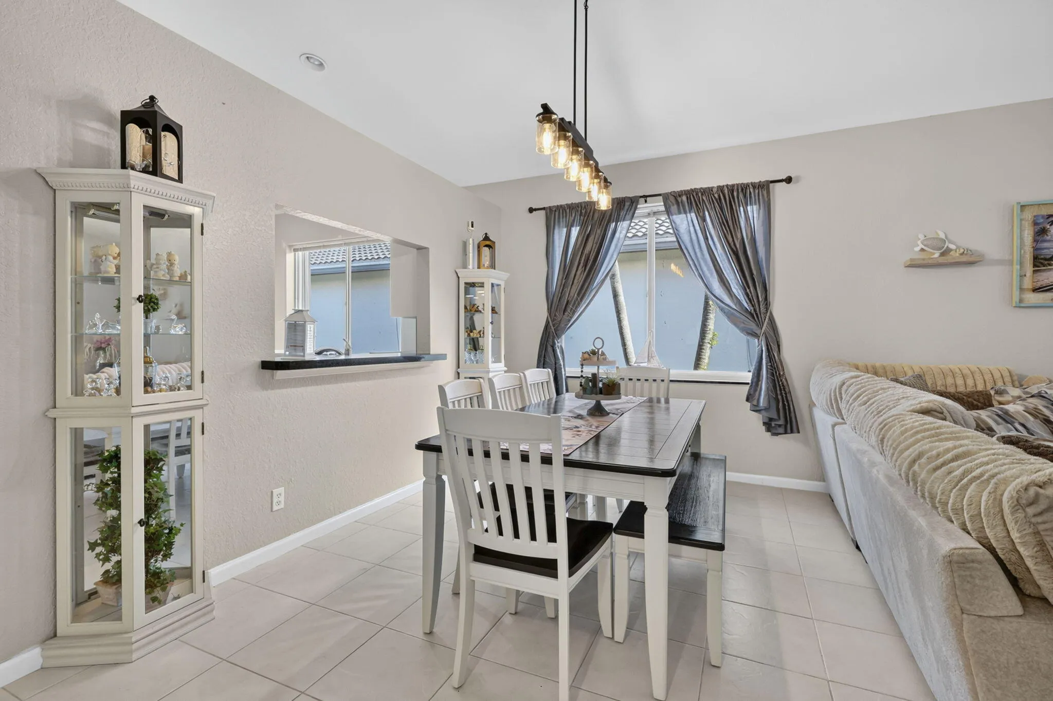 Open concept dining area featuring a pass-through window, white tile flooring, and a linear pendant light fixture