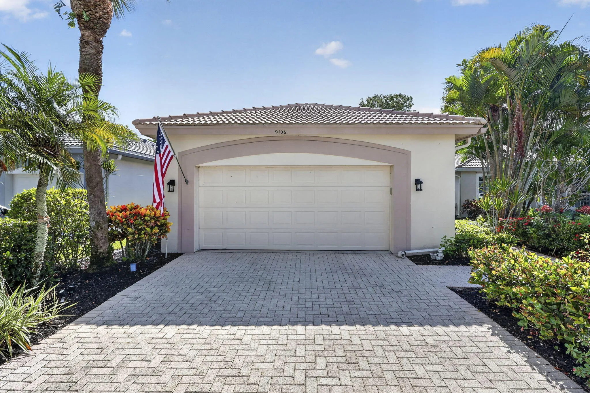 Stucco exterior with a tiled roof, paver driveway, and a two-car garage