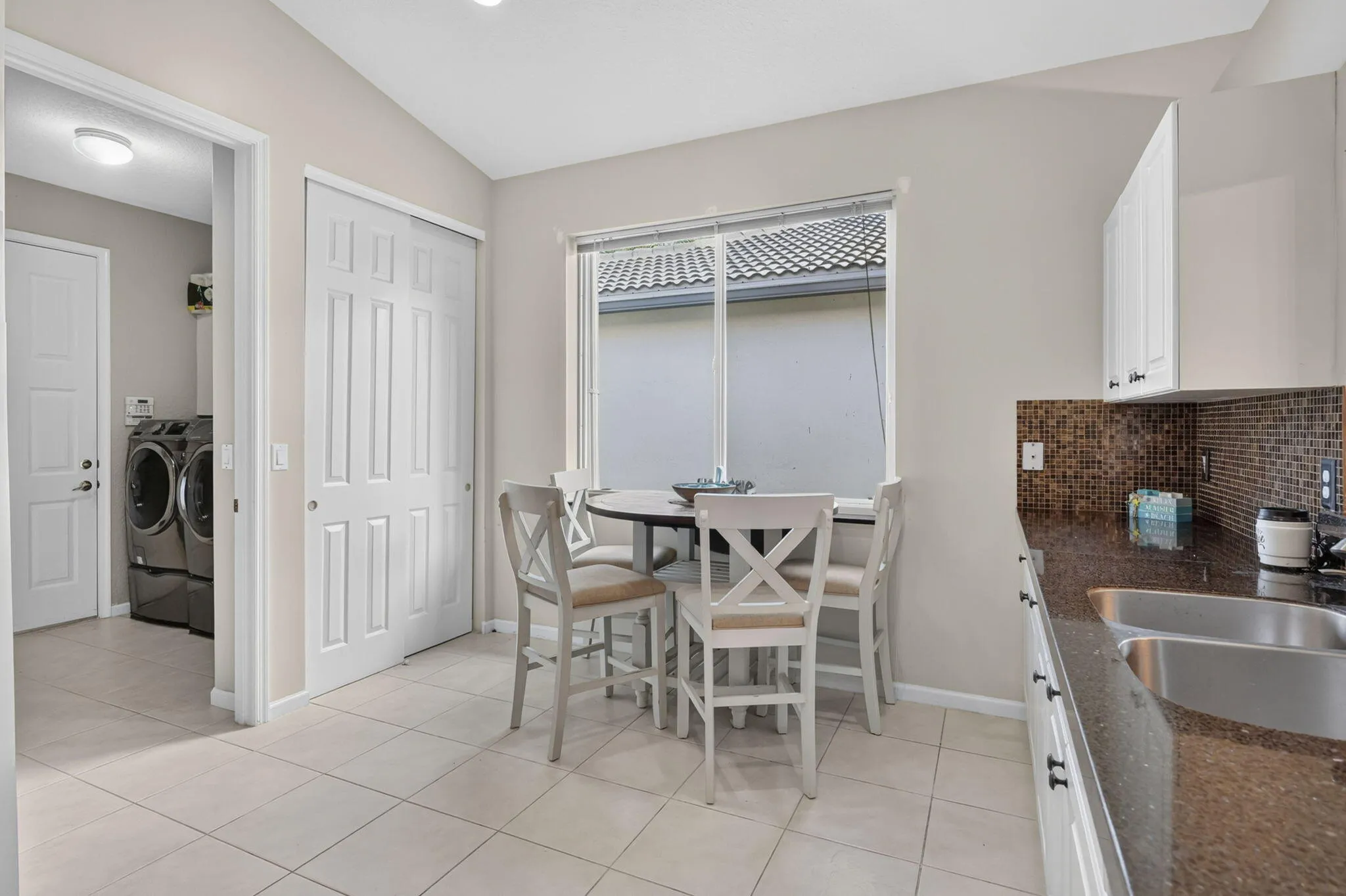 Kitchenette with tiled flooring, white cabinetry, a stainless steel sink, and a multi-tone tile backsplash