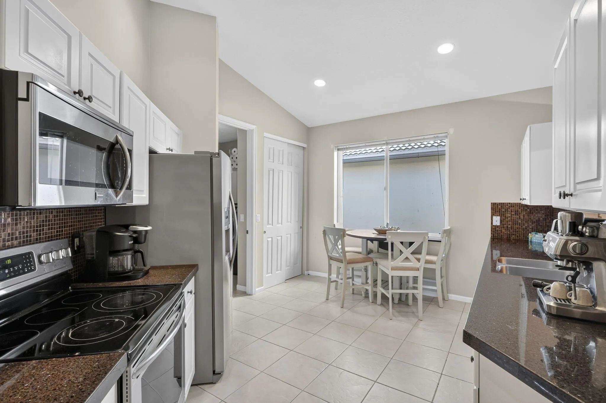 Kitchen featuring stainless steel appliances, white cabinetry, dark countertops, tiled backsplash, and recessed lighting