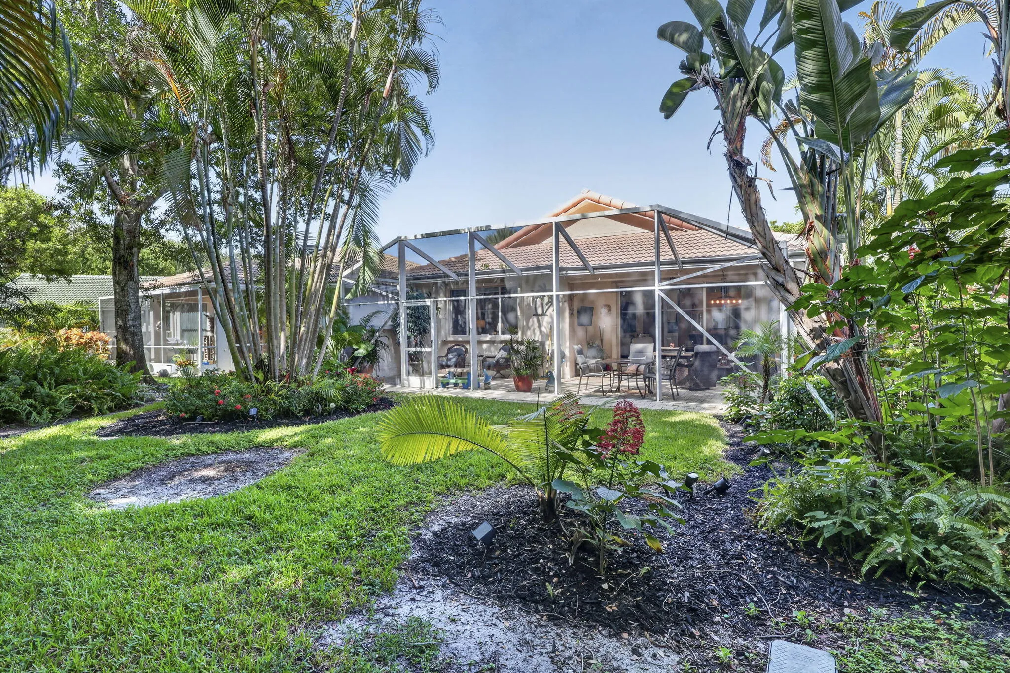 Lush landscaping with mature trees, screened-in patio, and tile roof