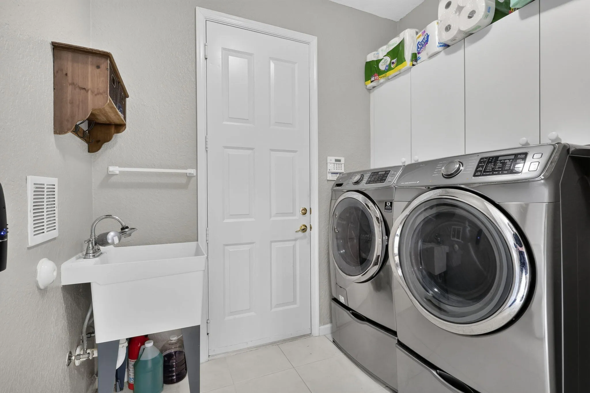 Laundry area featuring built-in cabinetry, durable tile flooring, and a utility sink