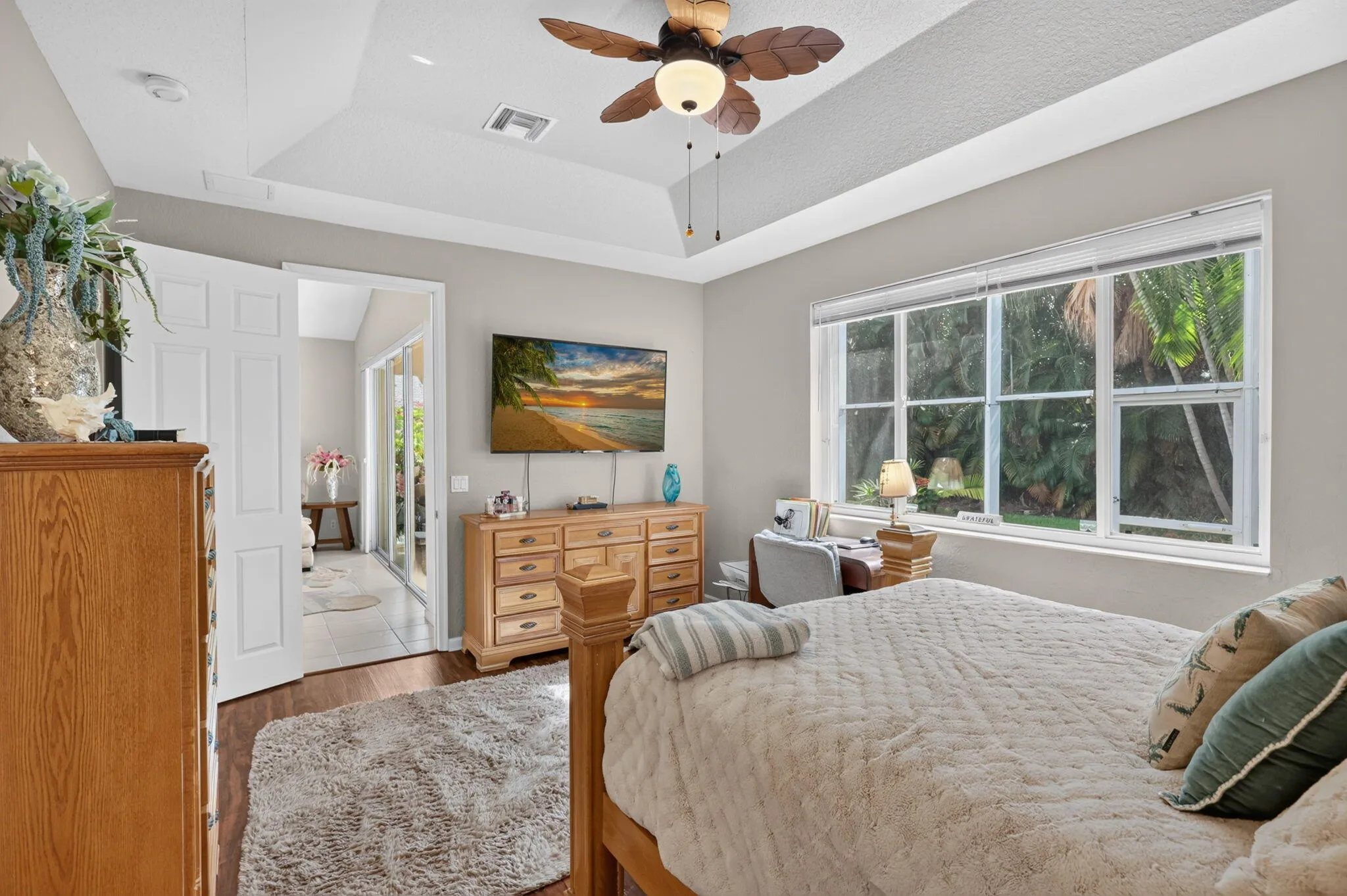 Tray ceiling with ceiling fan, wood-finish flooring, and expansive window with outdoor views