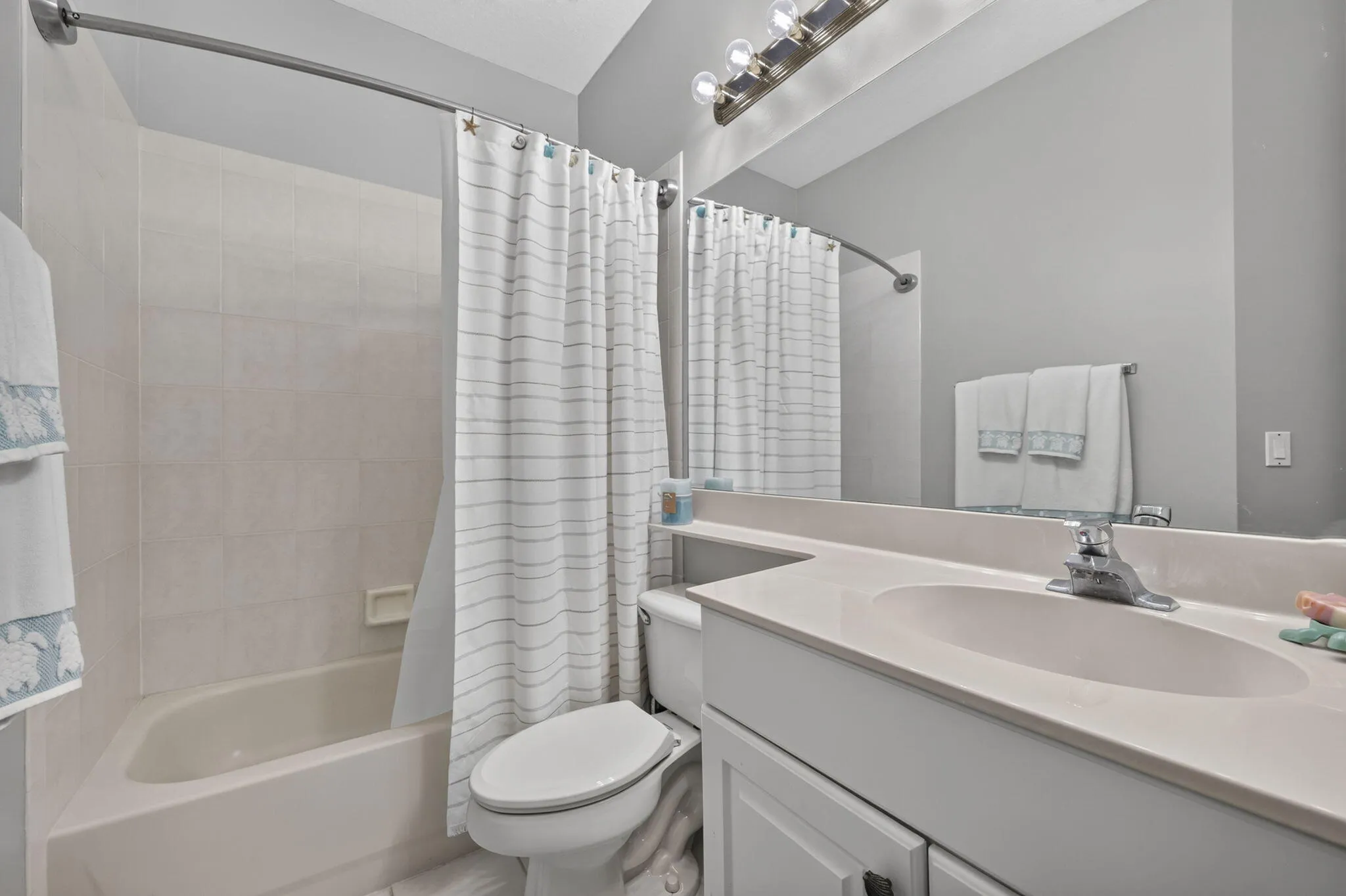 Built-in tub with tile surround, vanity with integrated sink, chrome faucet, and a large wall-mounted mirror