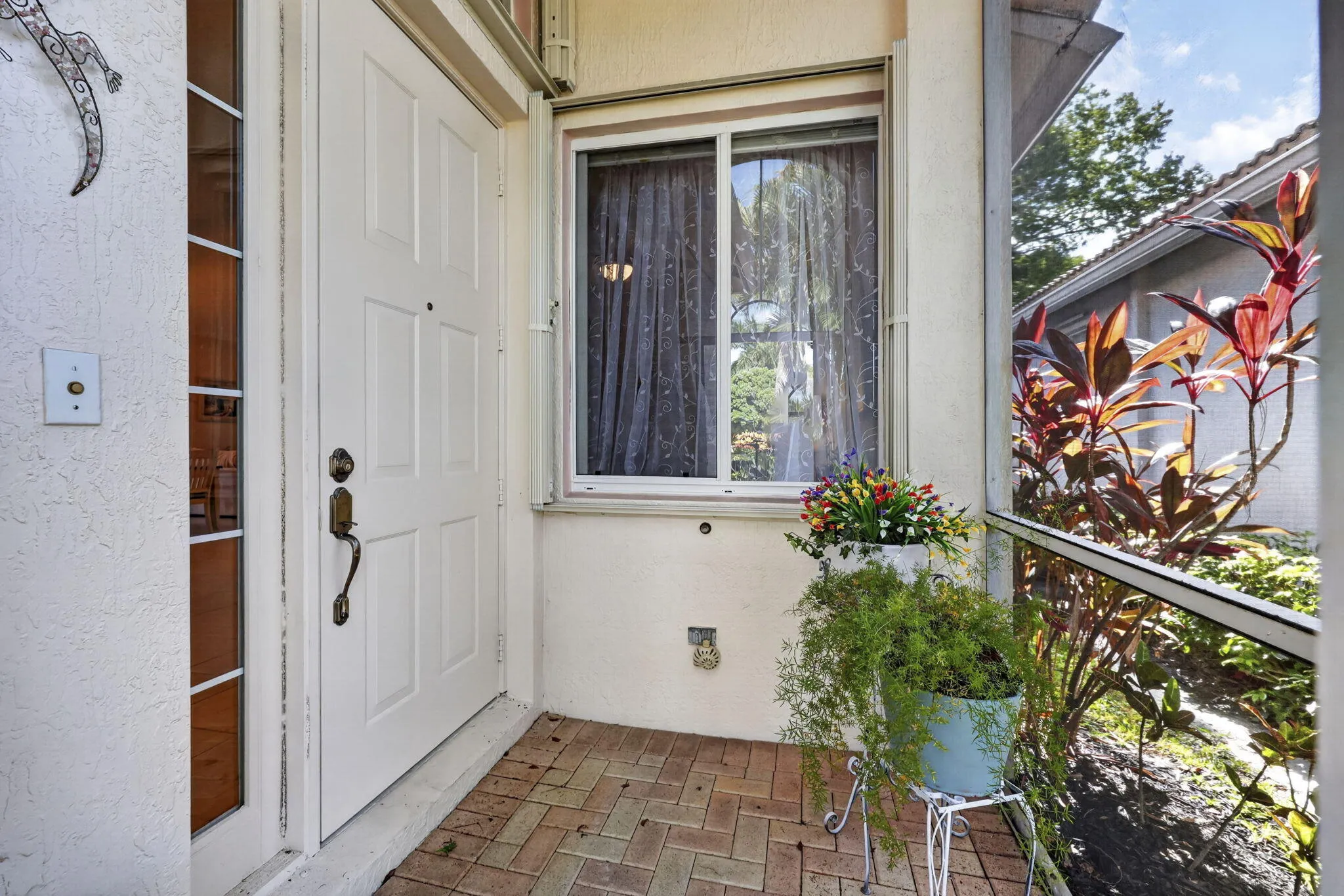 Panel door with sidelight, brick paver flooring, textured exterior finish, and screened enclosure