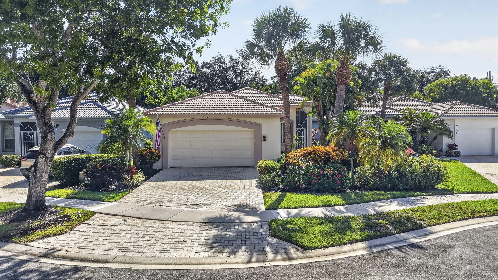 Elegant single-story residence showcasing a curved driveway with decorative paver hardscaping, two-car garage with paneled door, and arched roofline
