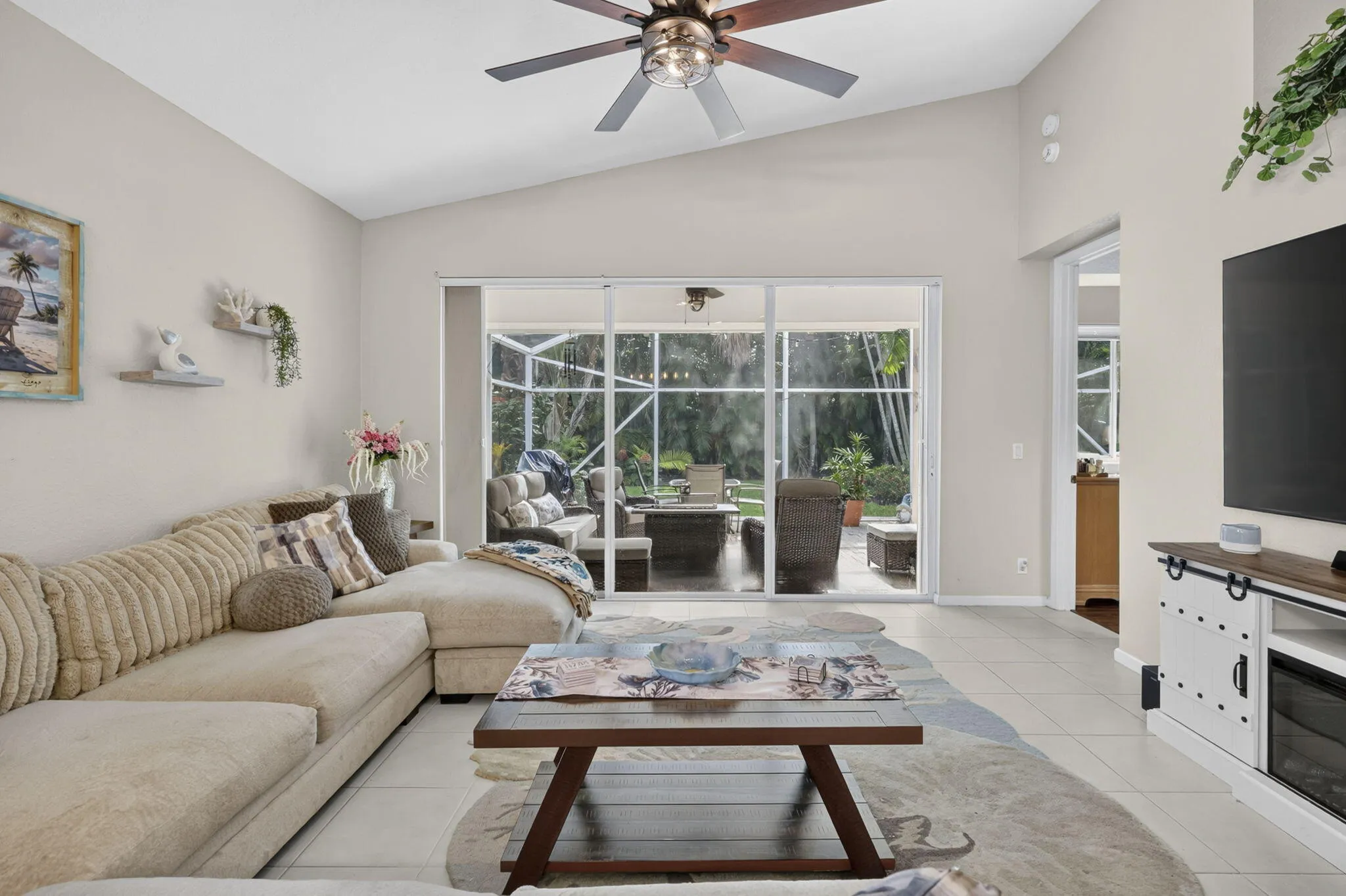 Vaulted ceilings with a ceiling fan, light-toned tile flooring, and sliding glass doors leading to an enclosed outdoor space