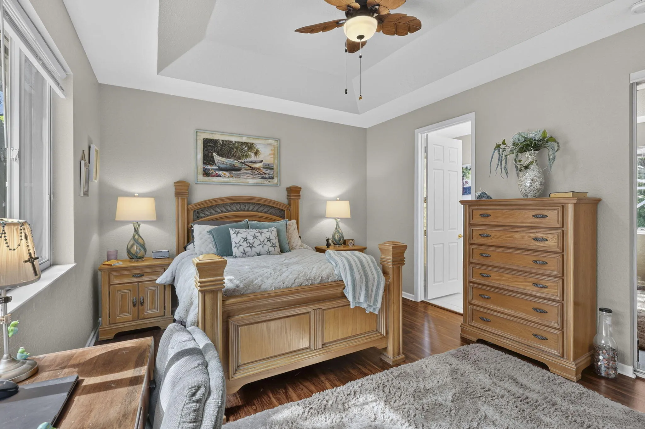 Tray ceiling with a ceiling fan, large window with blinds, wood-finish flooring, and white trim