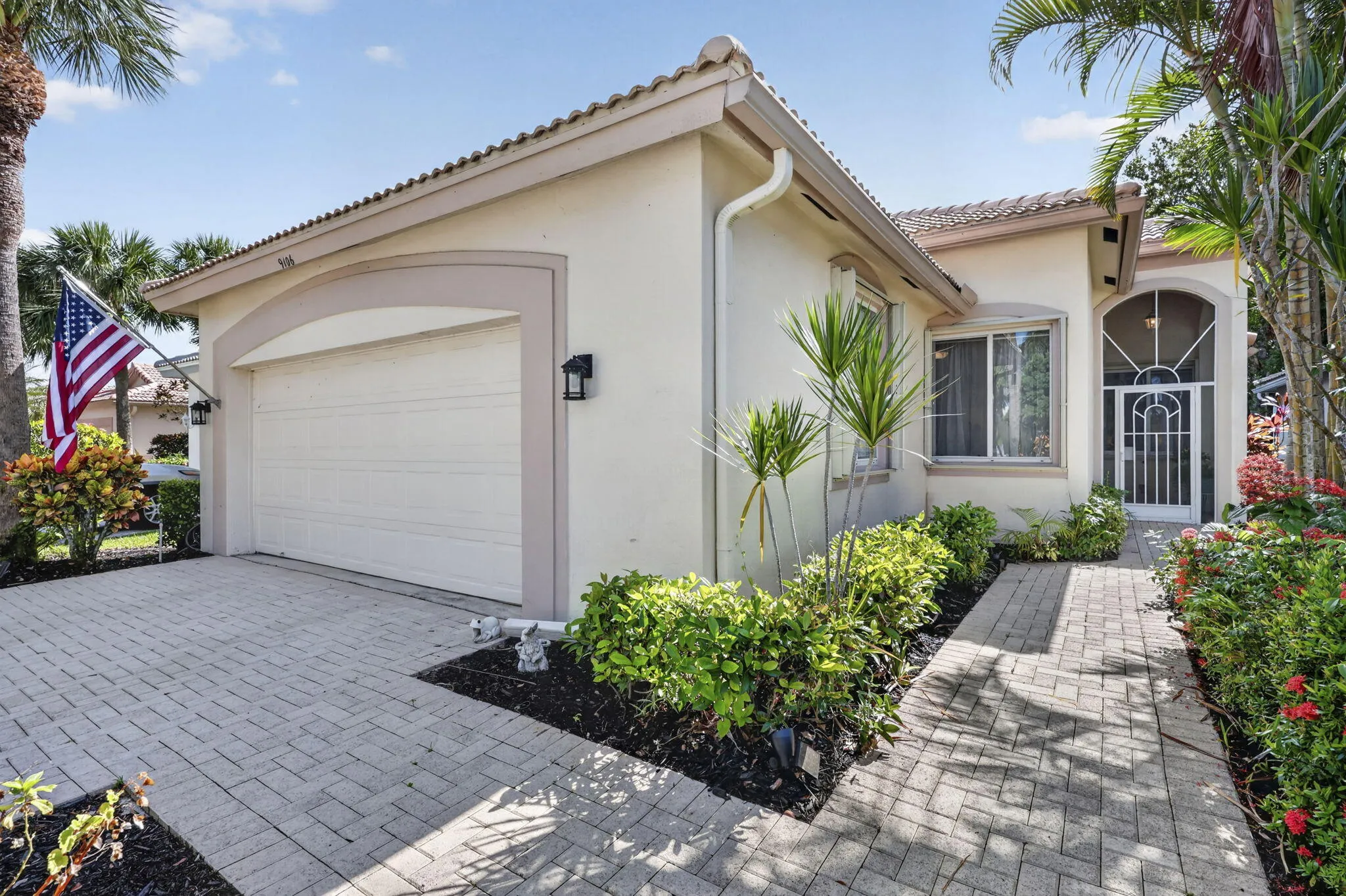 Stucco exterior with a tiled roof, paver driveway, arched garage door, paver walkway, and mature landscaping