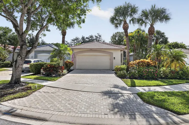 Paver driveway with a curved entry, lush landscaping, mature palm trees, arched entryway, and a tiled roof