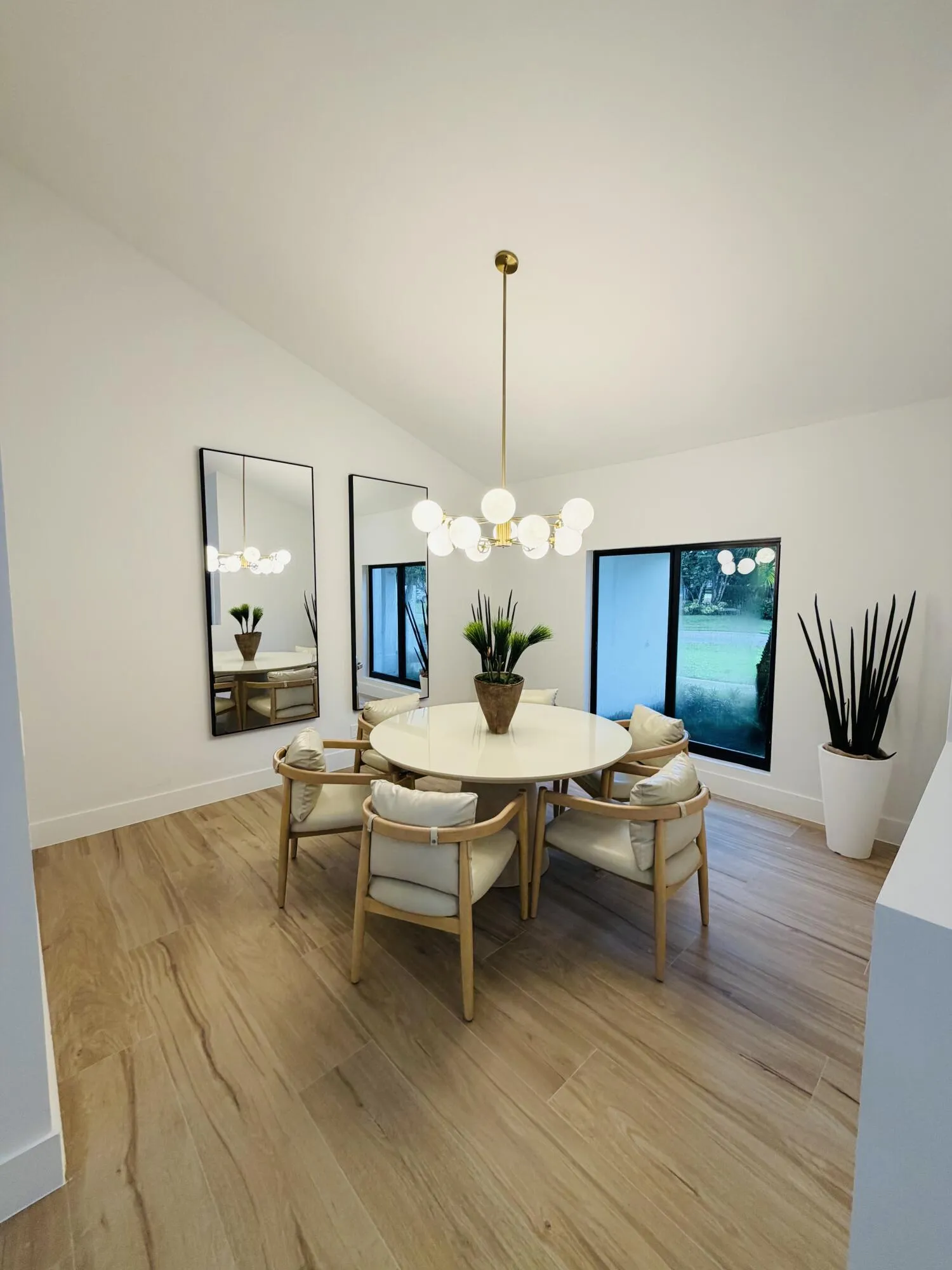Vaulted ceiling with a modern chandelier, wood-finish flooring, and large windows