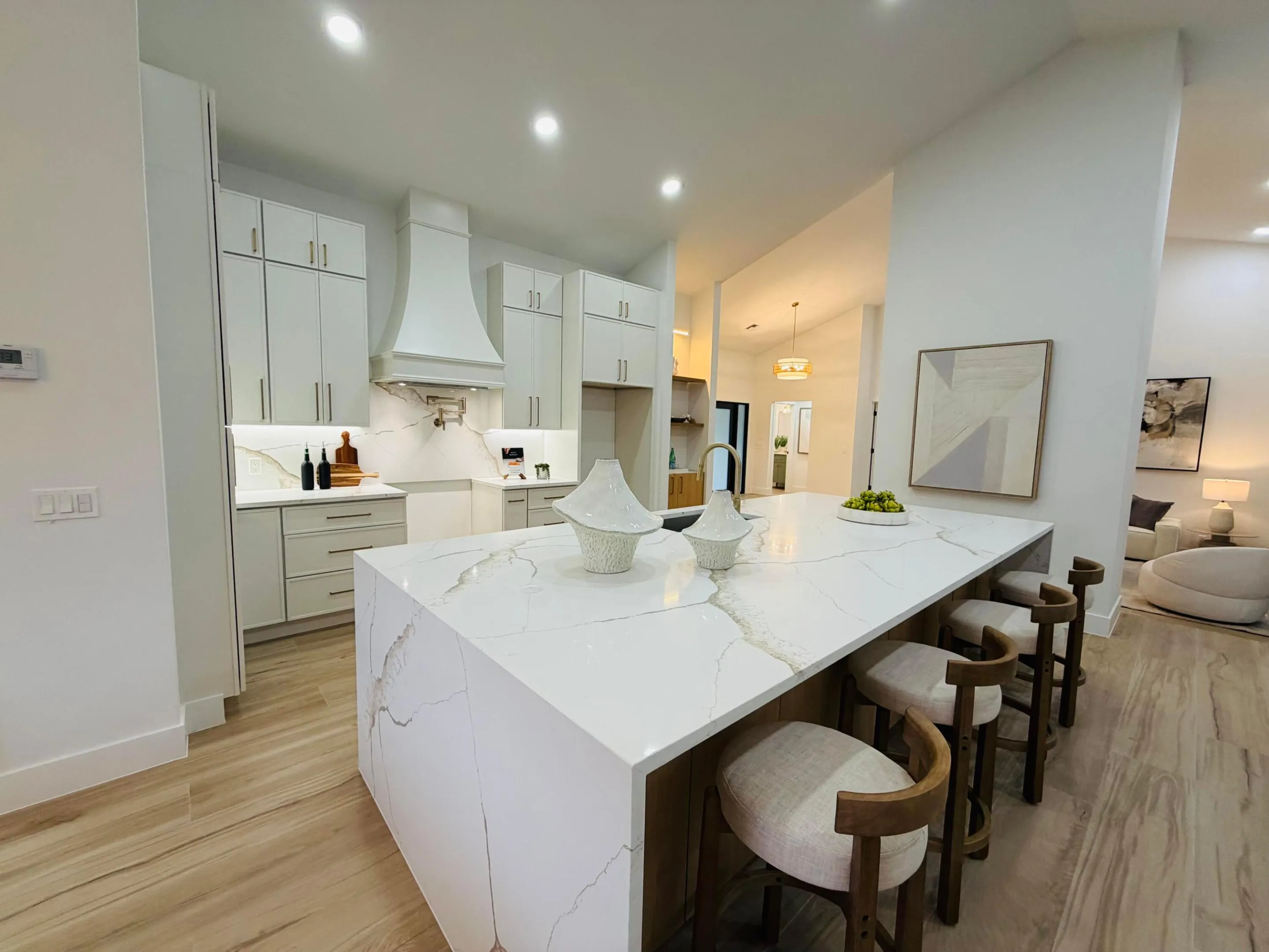 Spacious kitchen featuring a large island with seating, pendant lighting, light-toned cabinetry, and a designer range hood